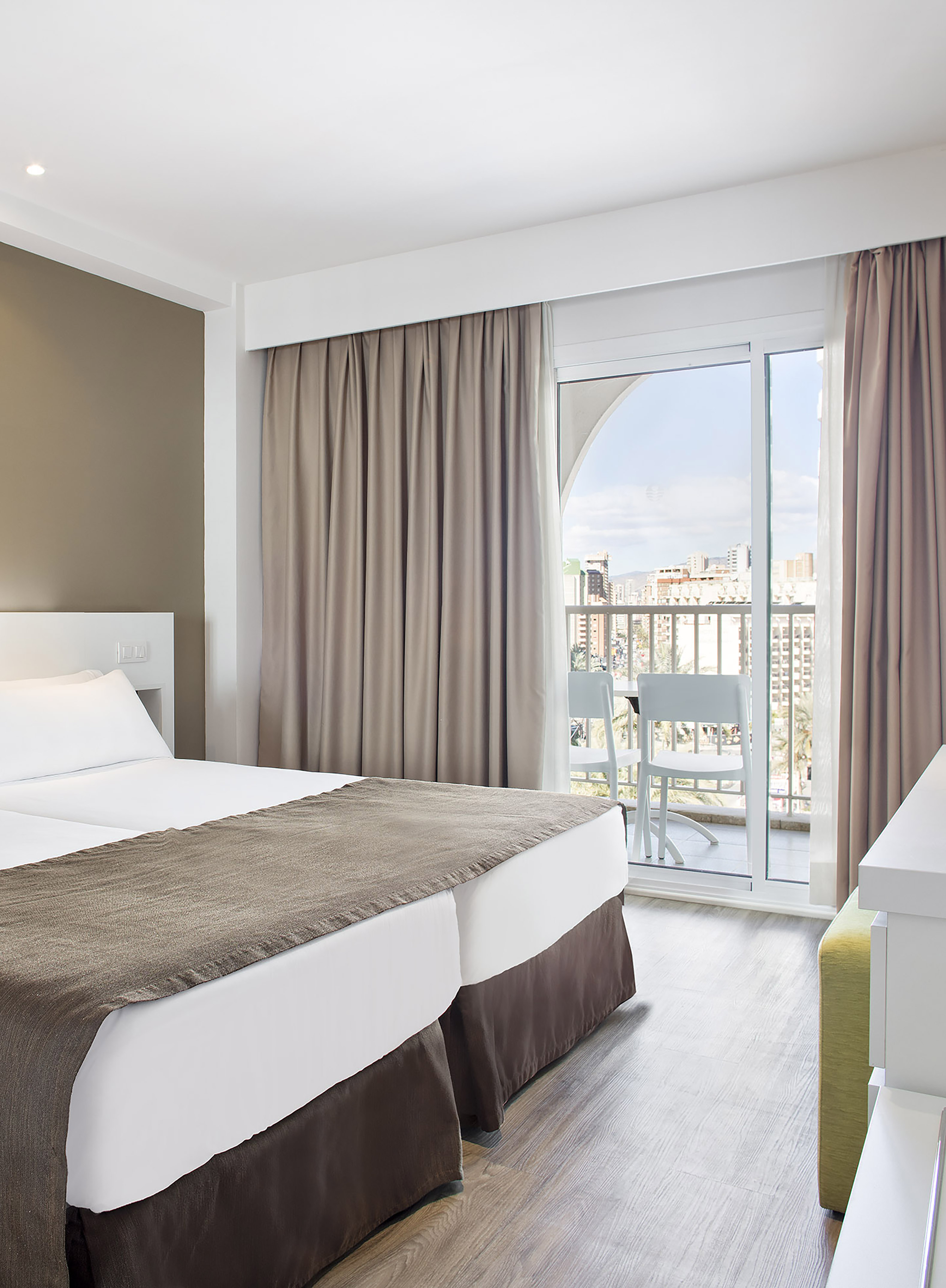 Modern hotel room with twin beds, balcony, and city view.