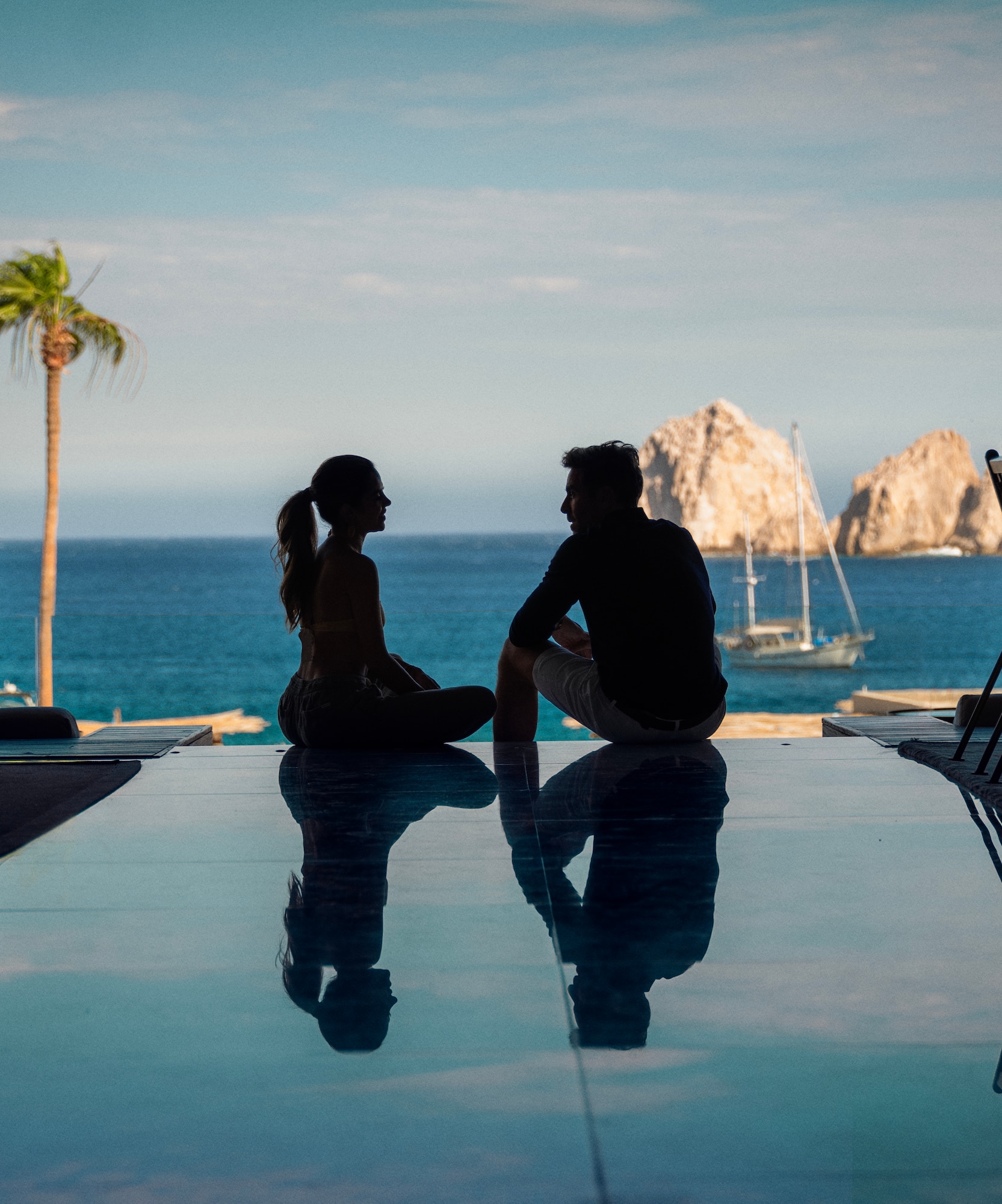 a man and woman sitting on a pool table with a body of water in the background