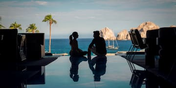 a man and woman sitting on a pool table with a body of water in the background