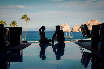 a man and woman sitting on a pool table with a body of water in the background