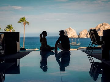 a man and woman sitting on a pool table with a body of water in the background