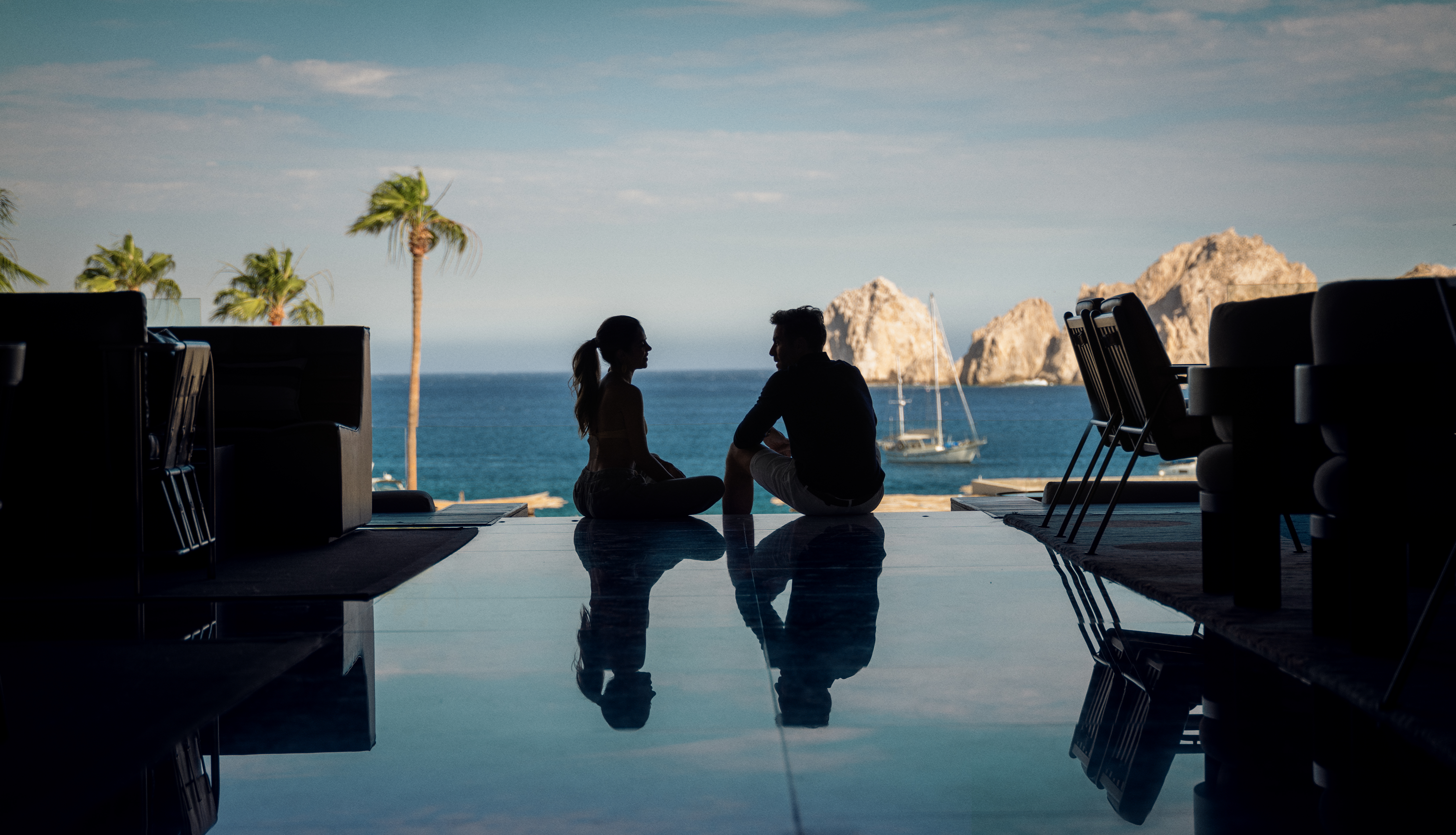 a man and woman sitting on a pool table with a body of water in the background