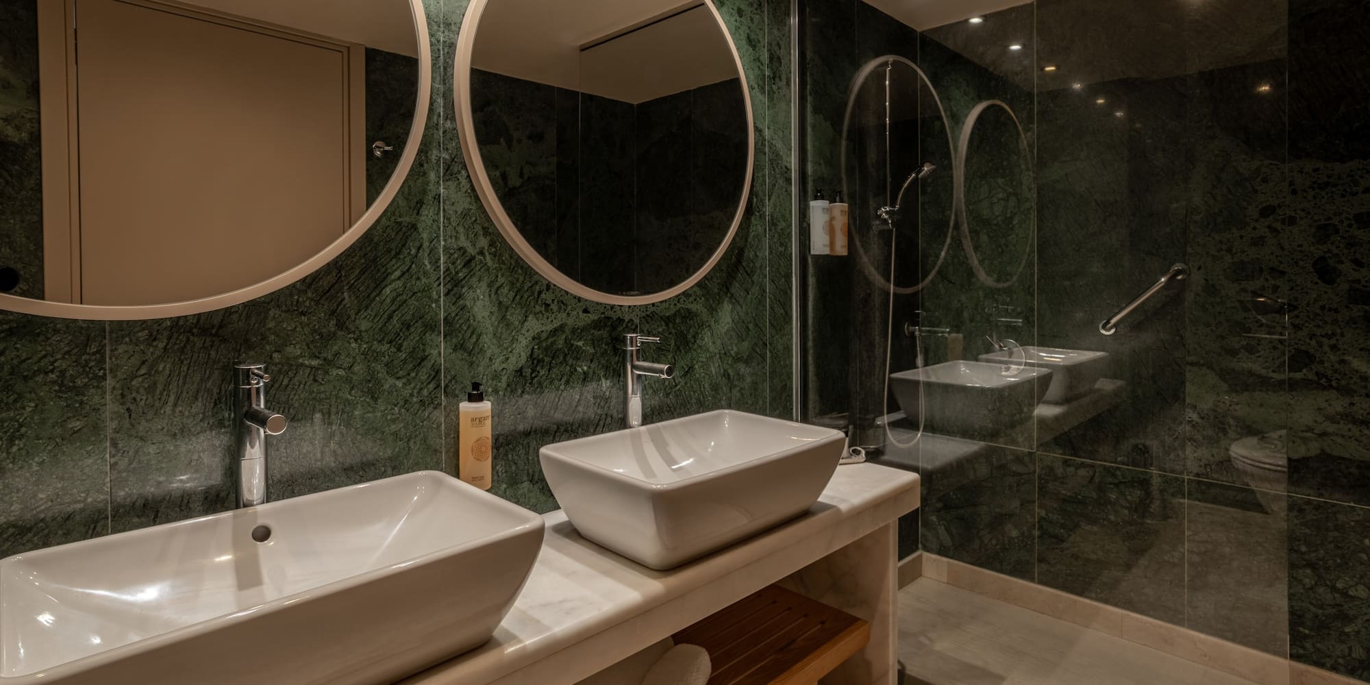 Luxury bathroom with green marble walls, double vessel sinks, and glass shower.