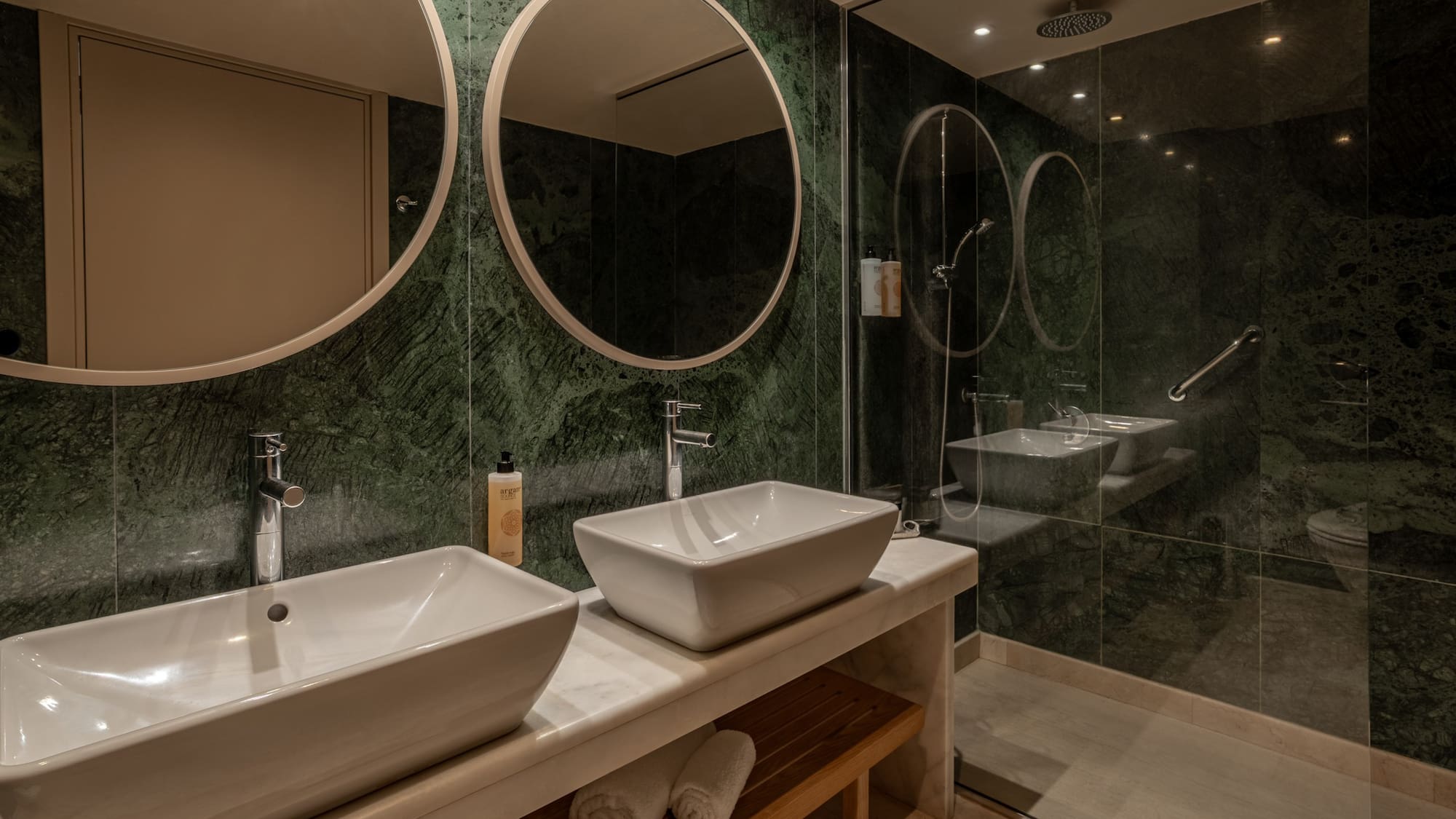 Luxury bathroom with green marble walls, double vessel sinks, and glass shower.
