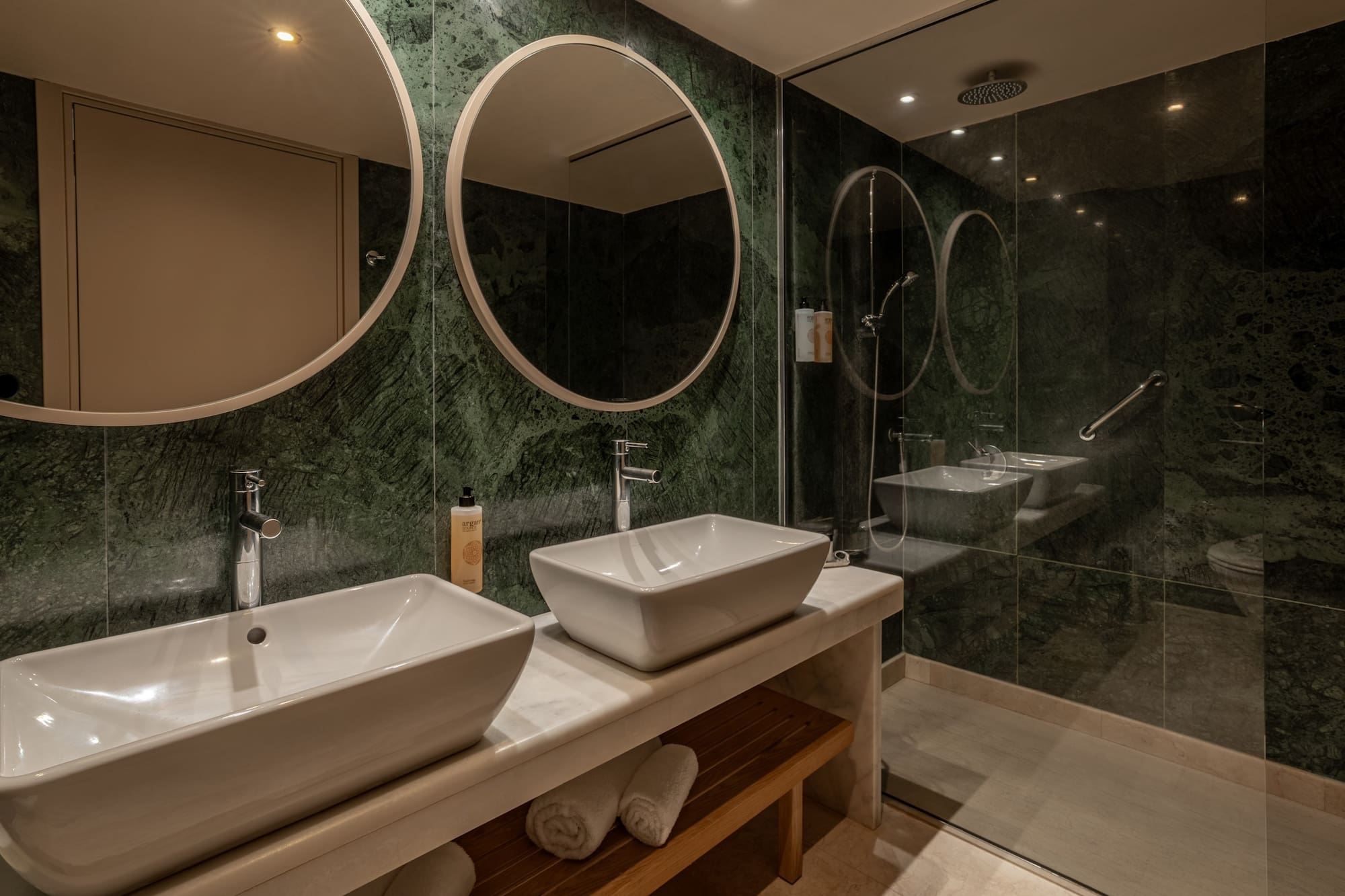 Luxury bathroom with green marble walls, double vessel sinks, and glass shower.