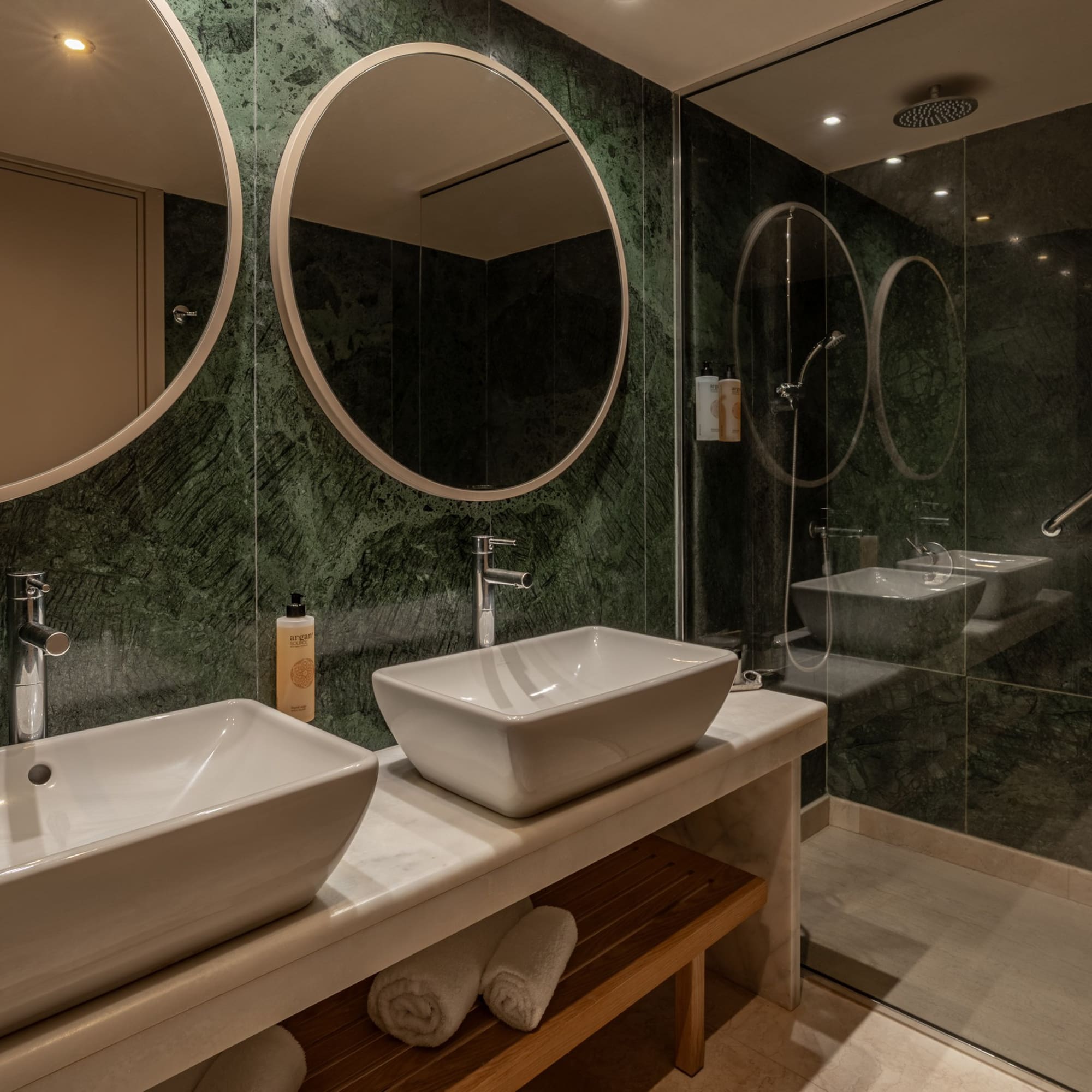Luxury bathroom with green marble walls, double vessel sinks, and glass shower.