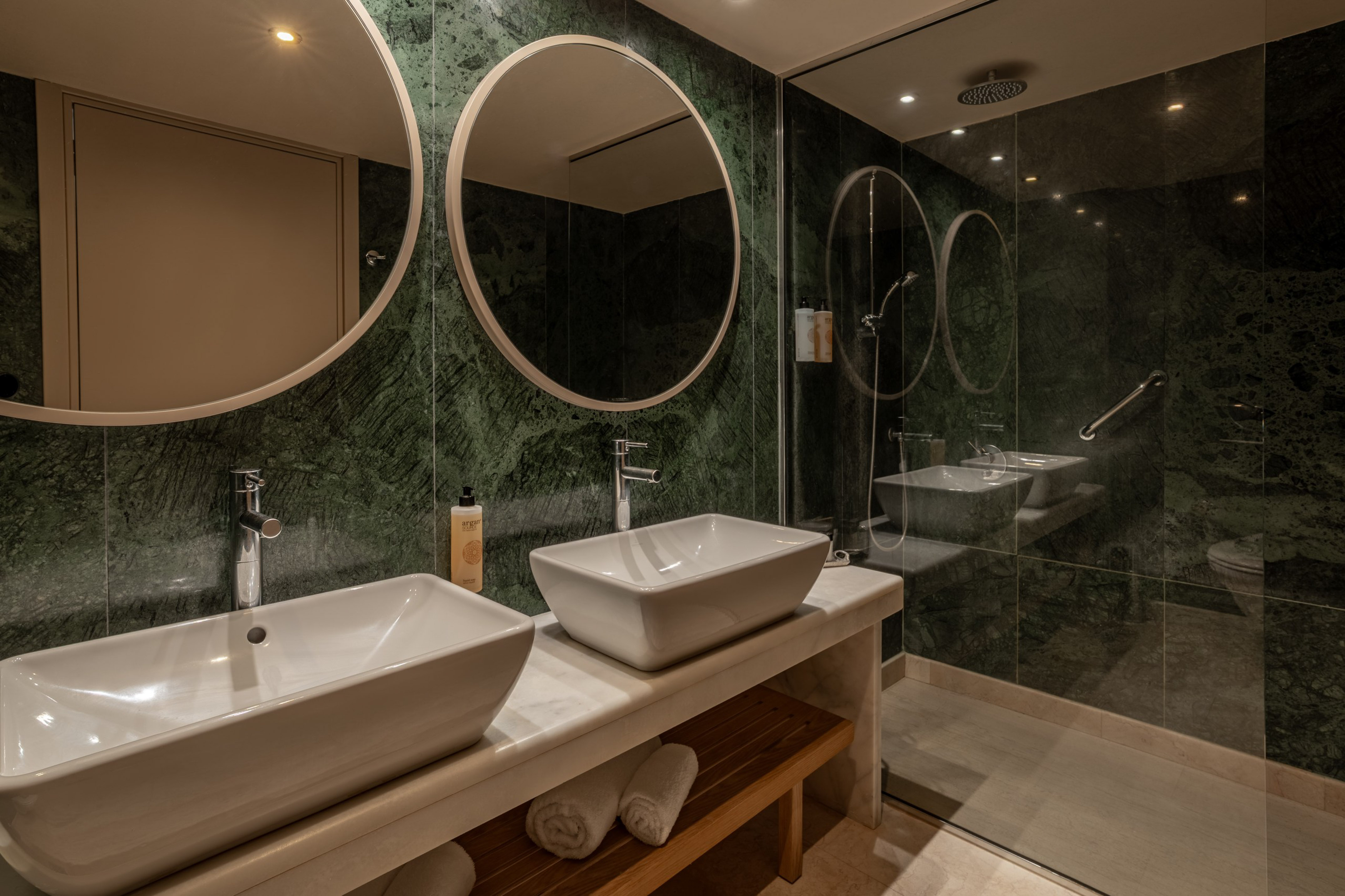 Luxury bathroom with green marble walls, double vessel sinks, and glass shower.