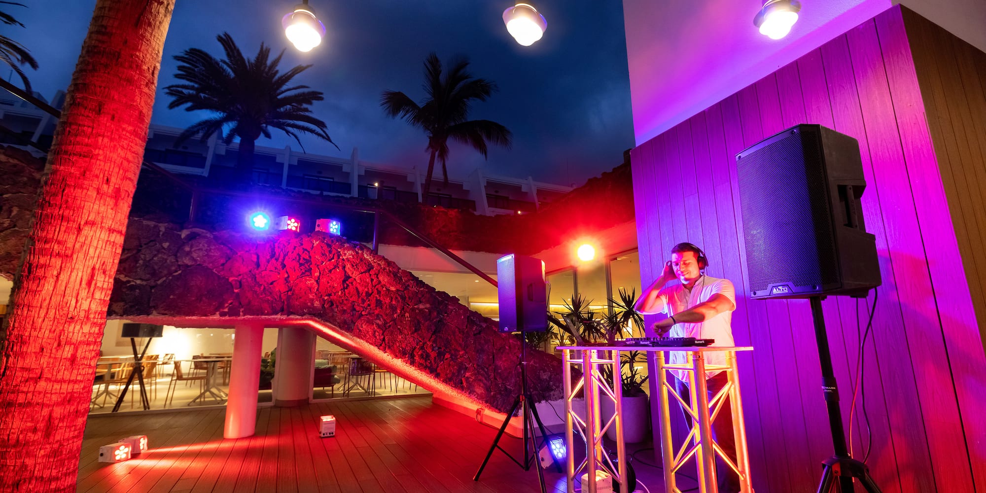 a man standing on a stage with a speaker and a building with trees