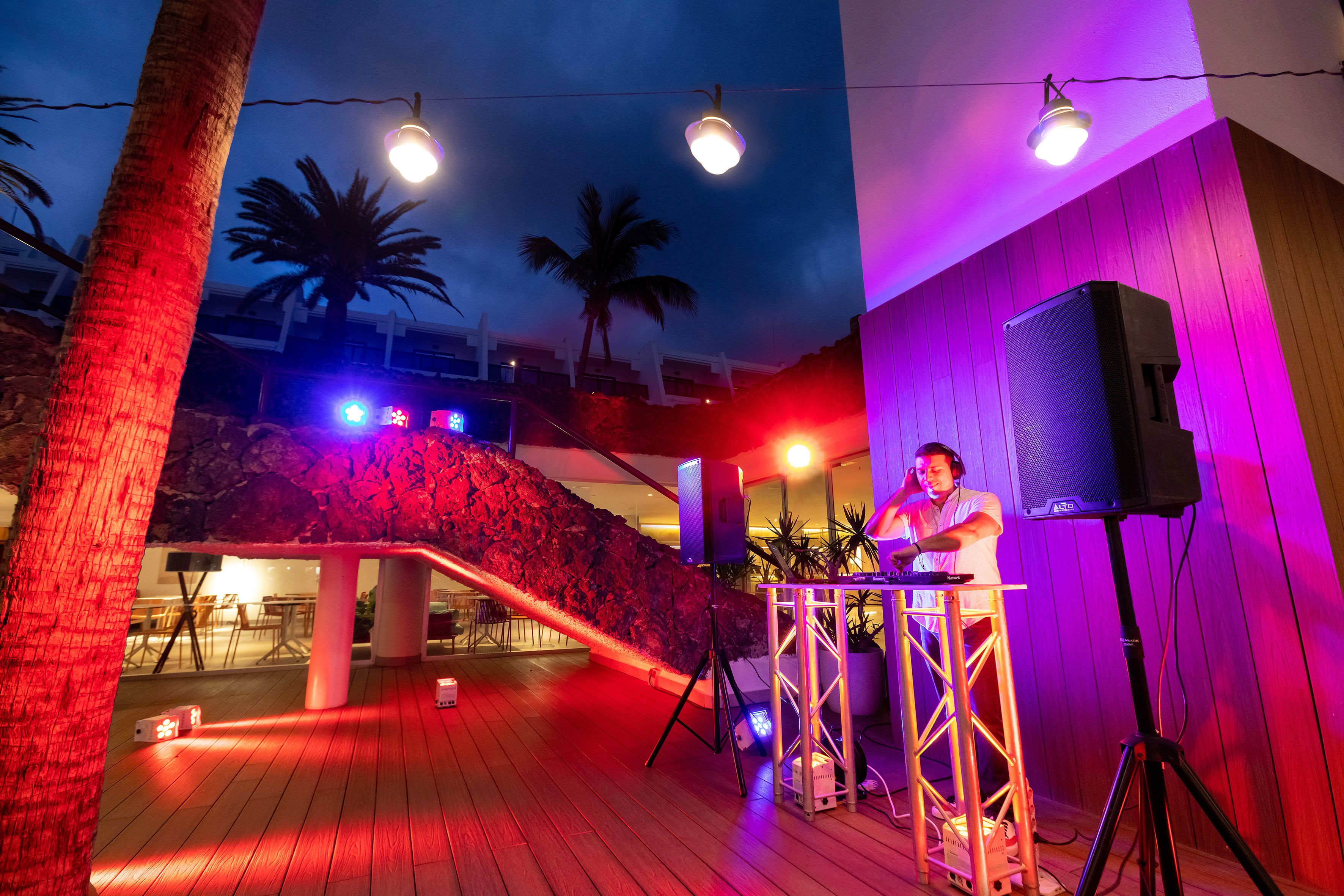 a man standing on a stage with a speaker and a building with trees