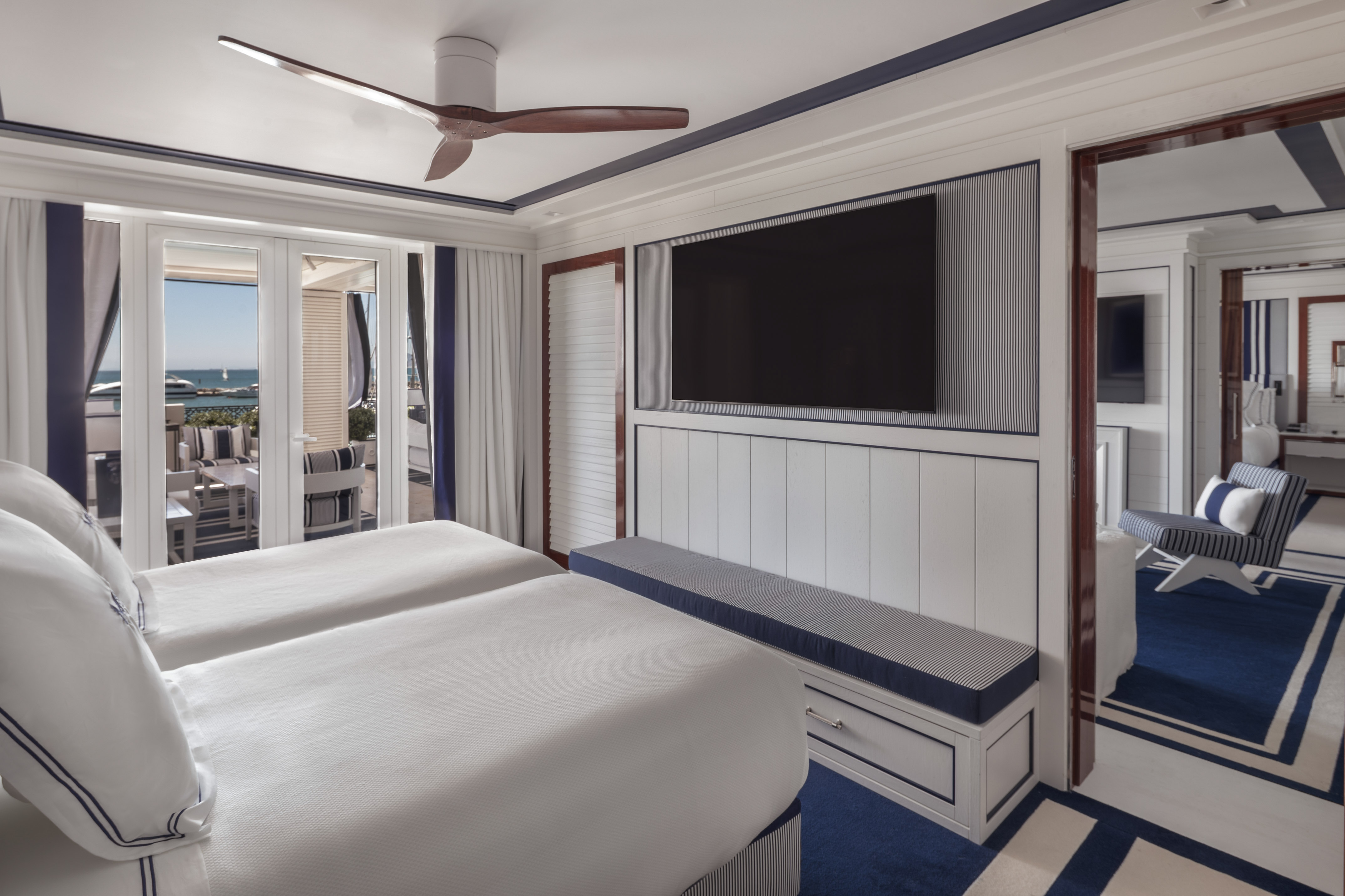 Nautical hotel bedroom, twin beds, sea view balcony, blue decor, wall TV.