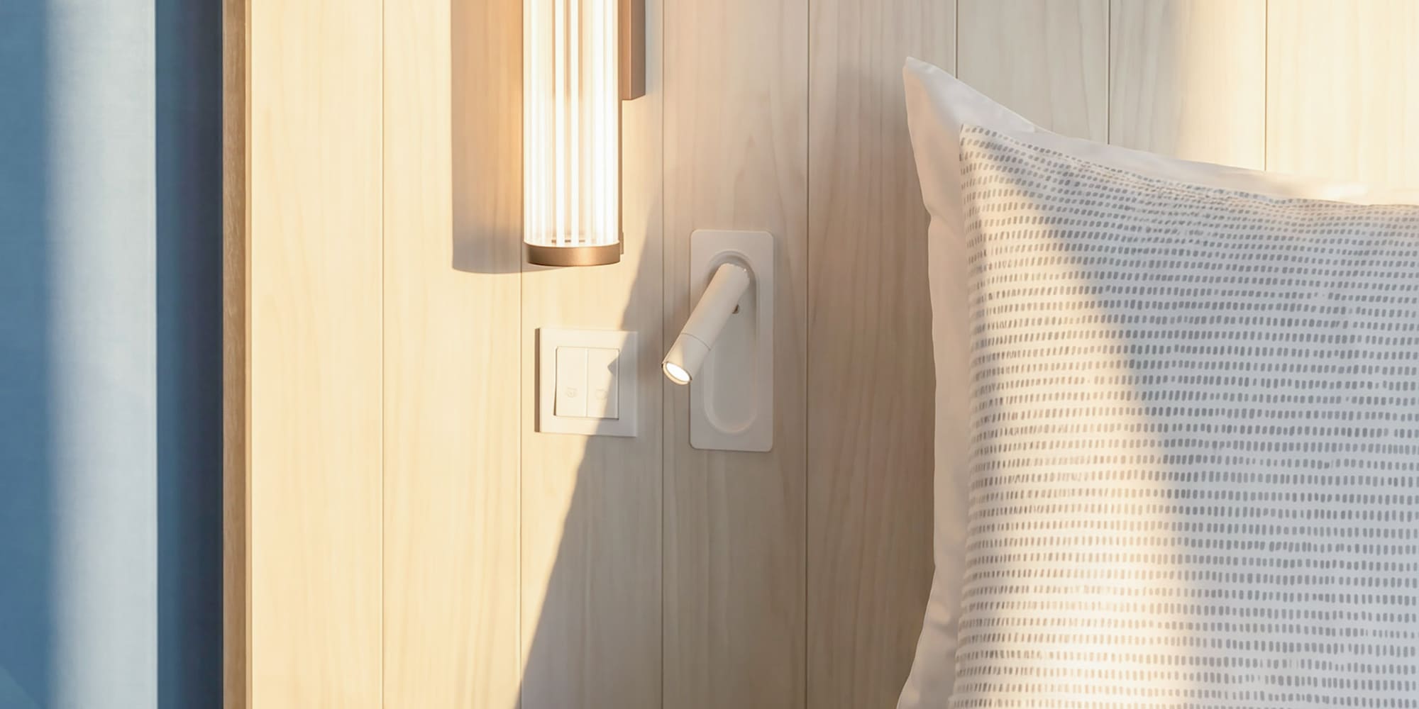 Modern bedroom with wooden headboard, sleek lighting, and a teal rotary phone.