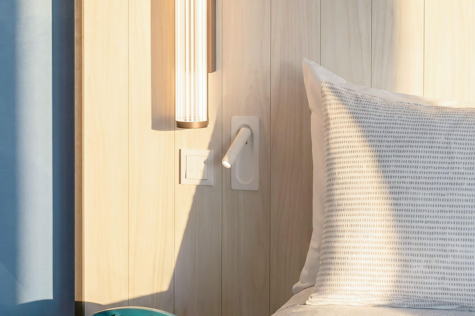 Modern bedroom with wooden headboard, sleek lighting, and a teal rotary phone.