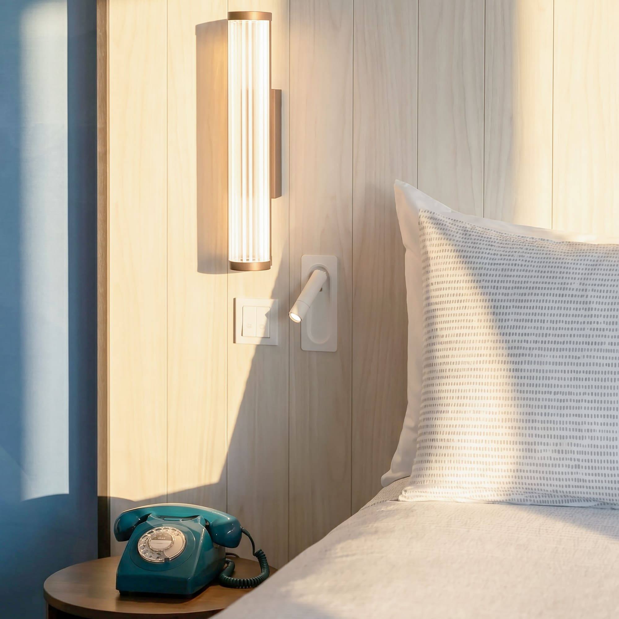 Modern bedroom with wooden headboard, sleek lighting, and a teal rotary phone.
