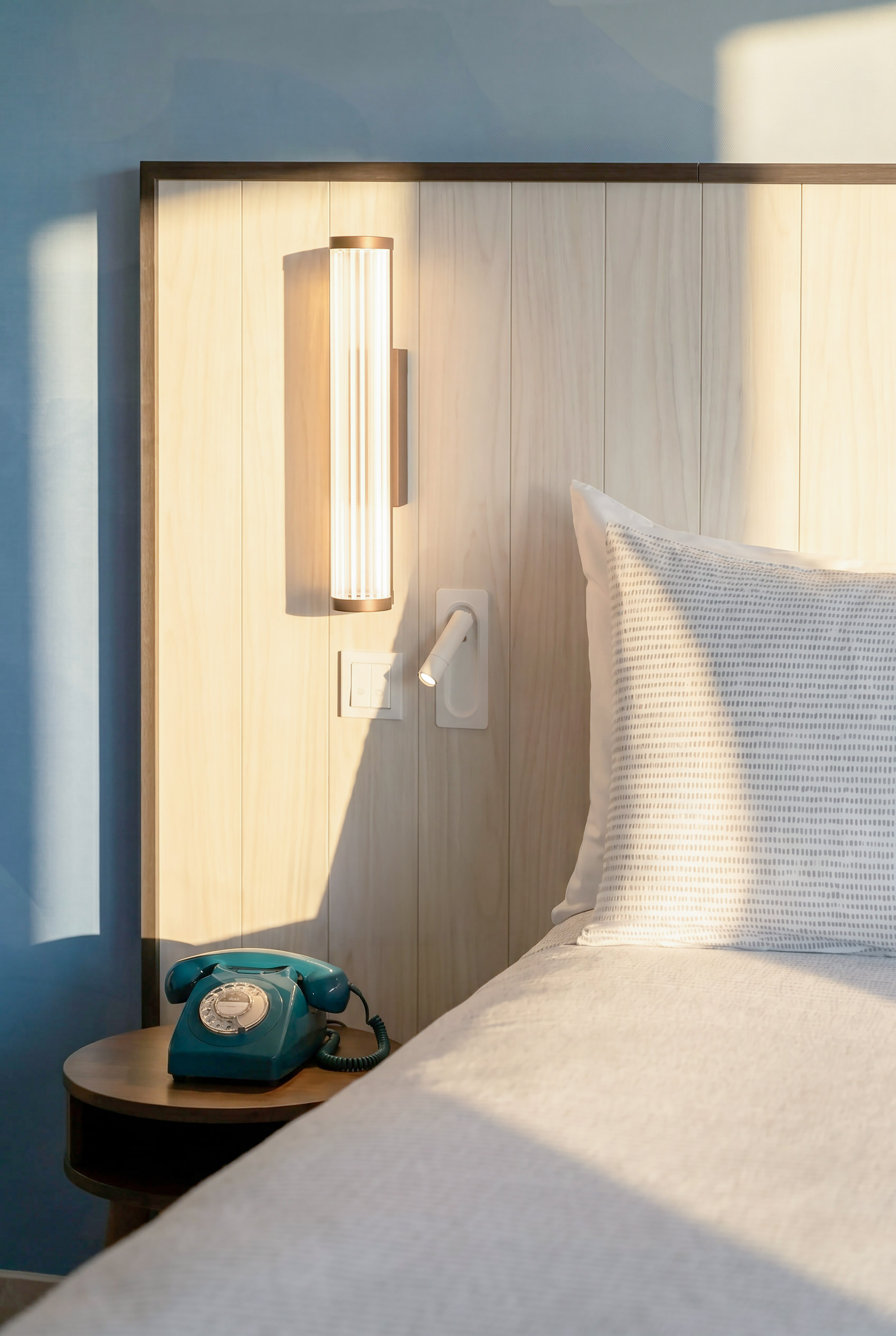 Modern bedroom with wooden headboard, sleek lighting, and a teal rotary phone.