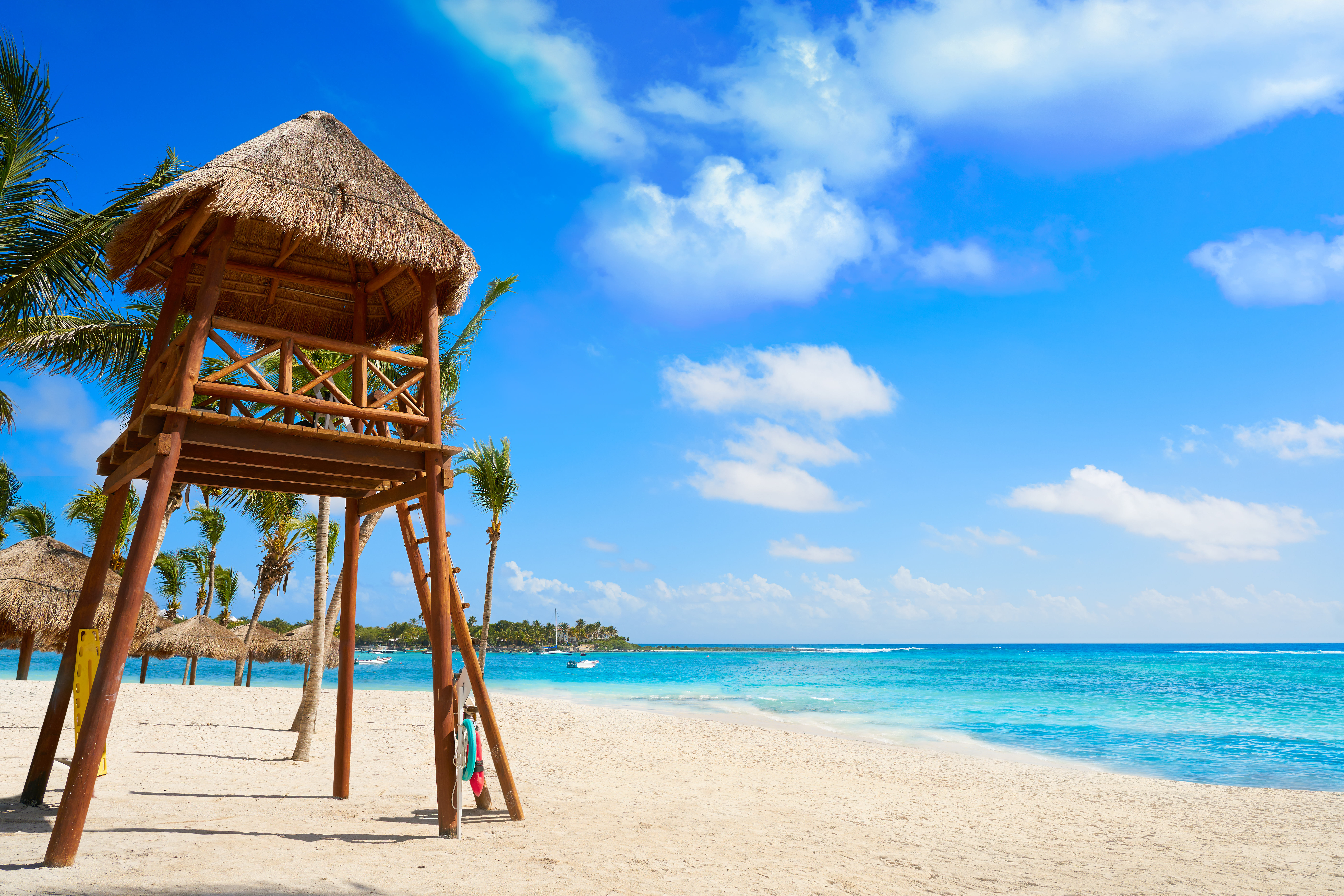 Playa caribeña con torre salvavidas, arena blanca, mar turquesa y palmeras.