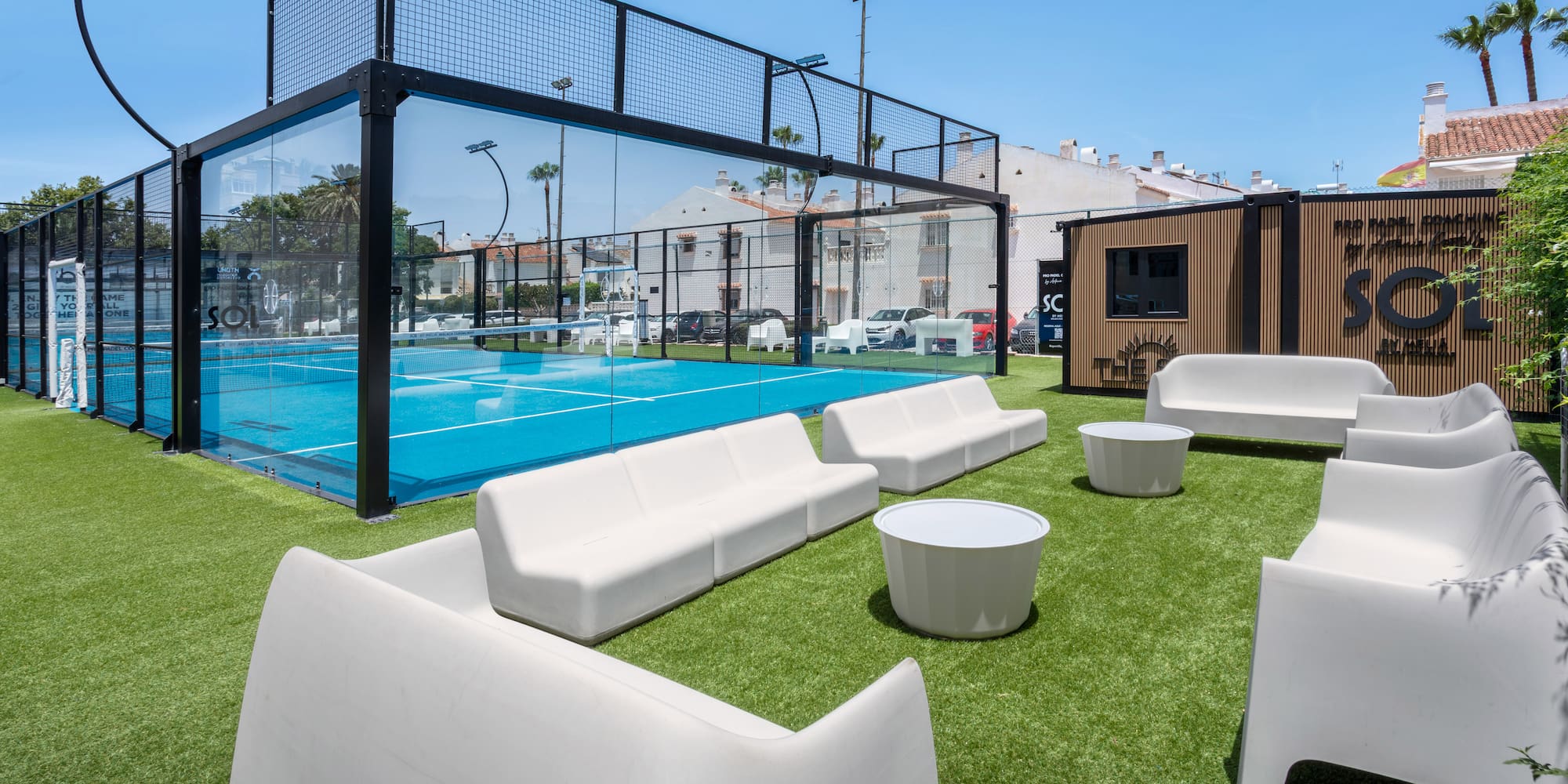 Modern blue padel court with artificial turf and white outdoor lounge area.