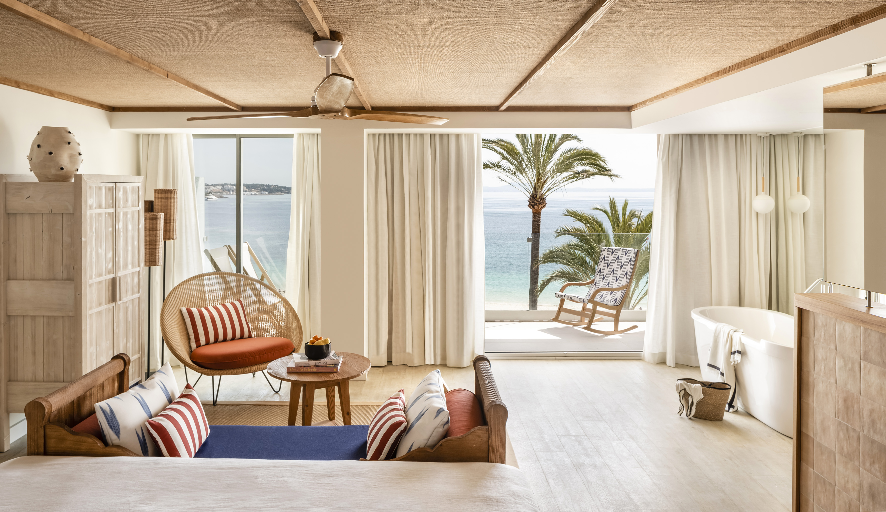 Luxury oceanfront suite with balcony, palm trees, and a freestanding tub.