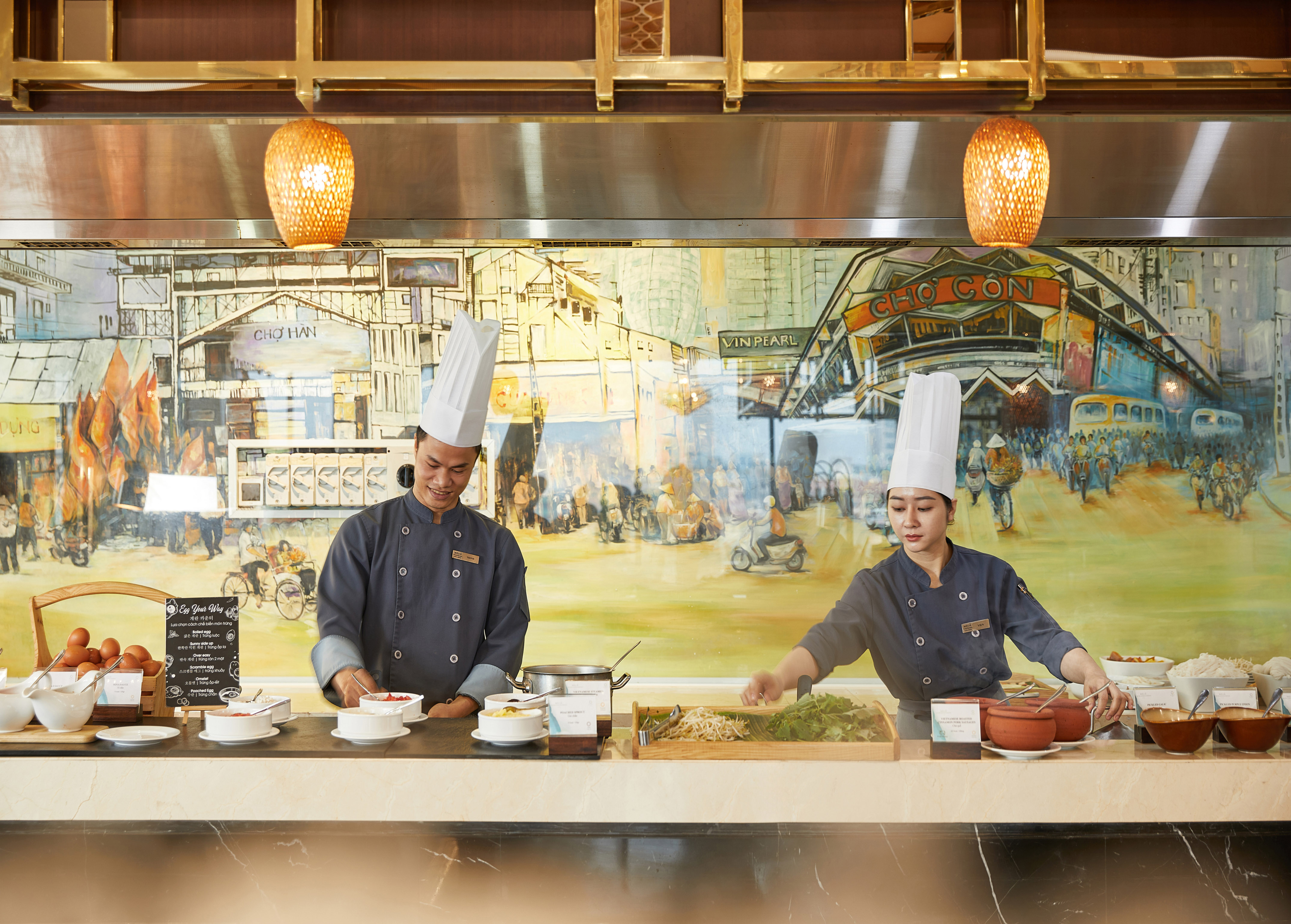 Vietnamese chefs preparing fresh food at a hotel buffet with market mural.