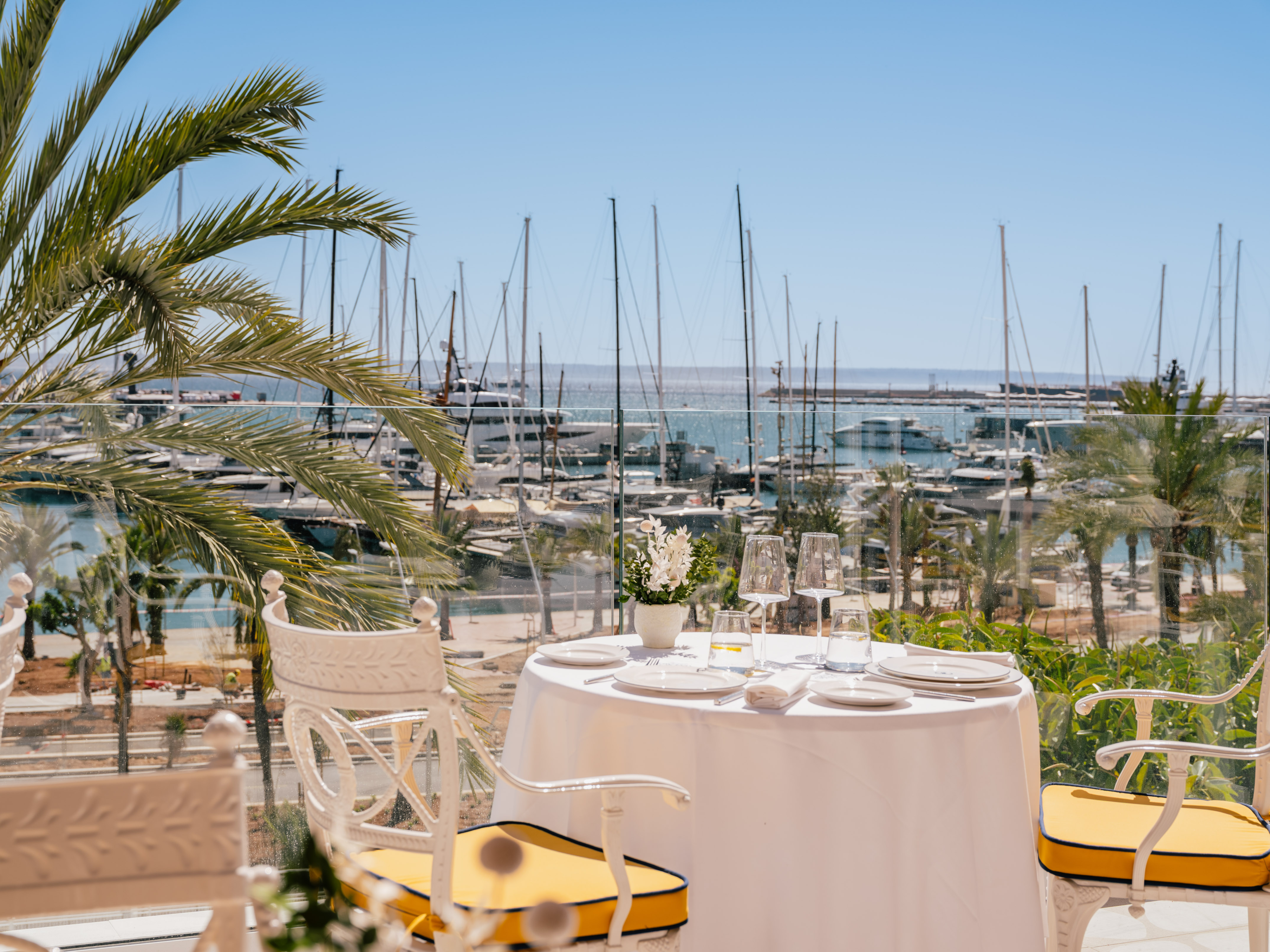 Restaurant dining table on terrace with marina and yacht view.
