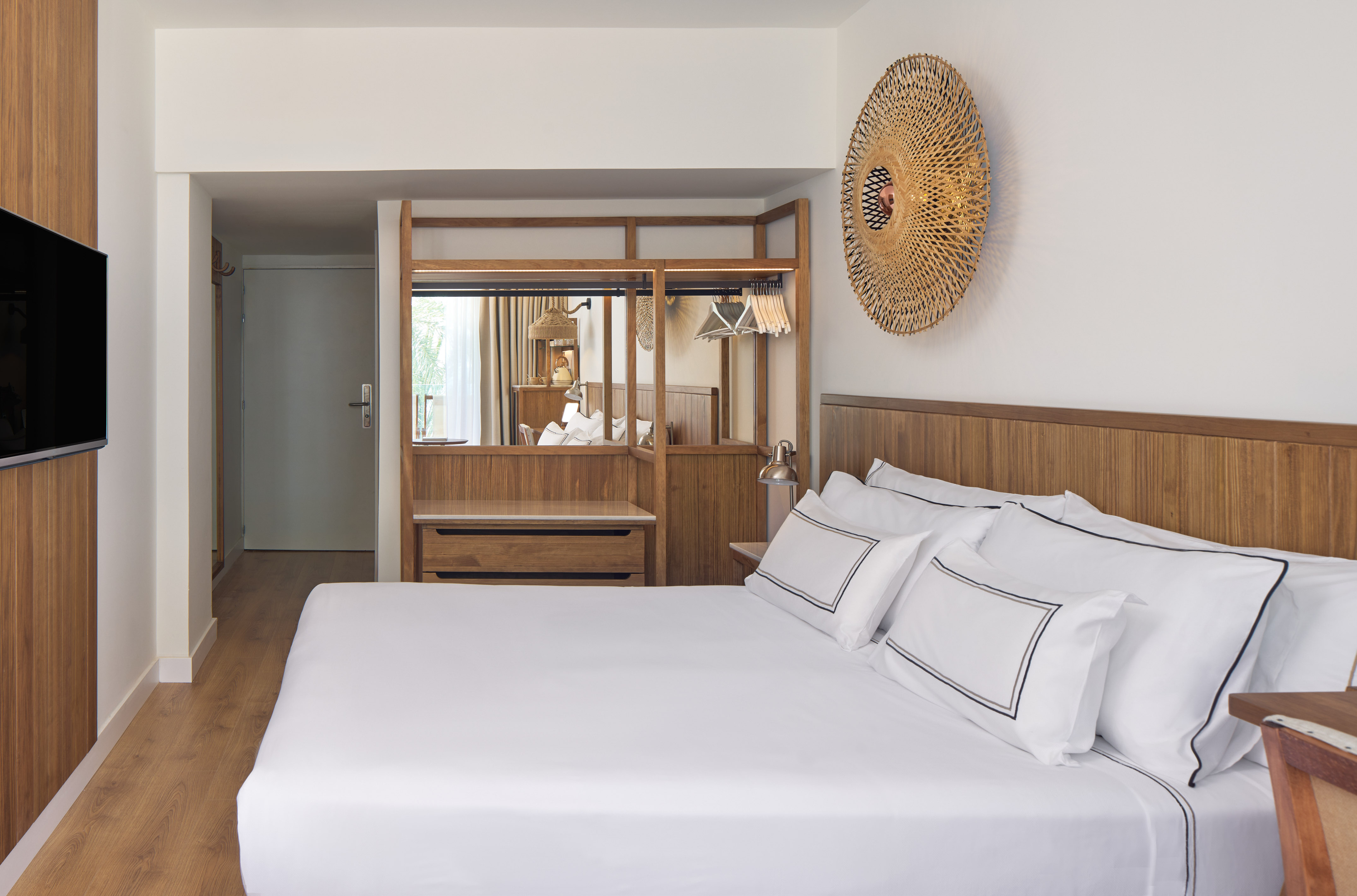Modern hotel bedroom with white bed, wooden furniture, TV, and woven wall decor.