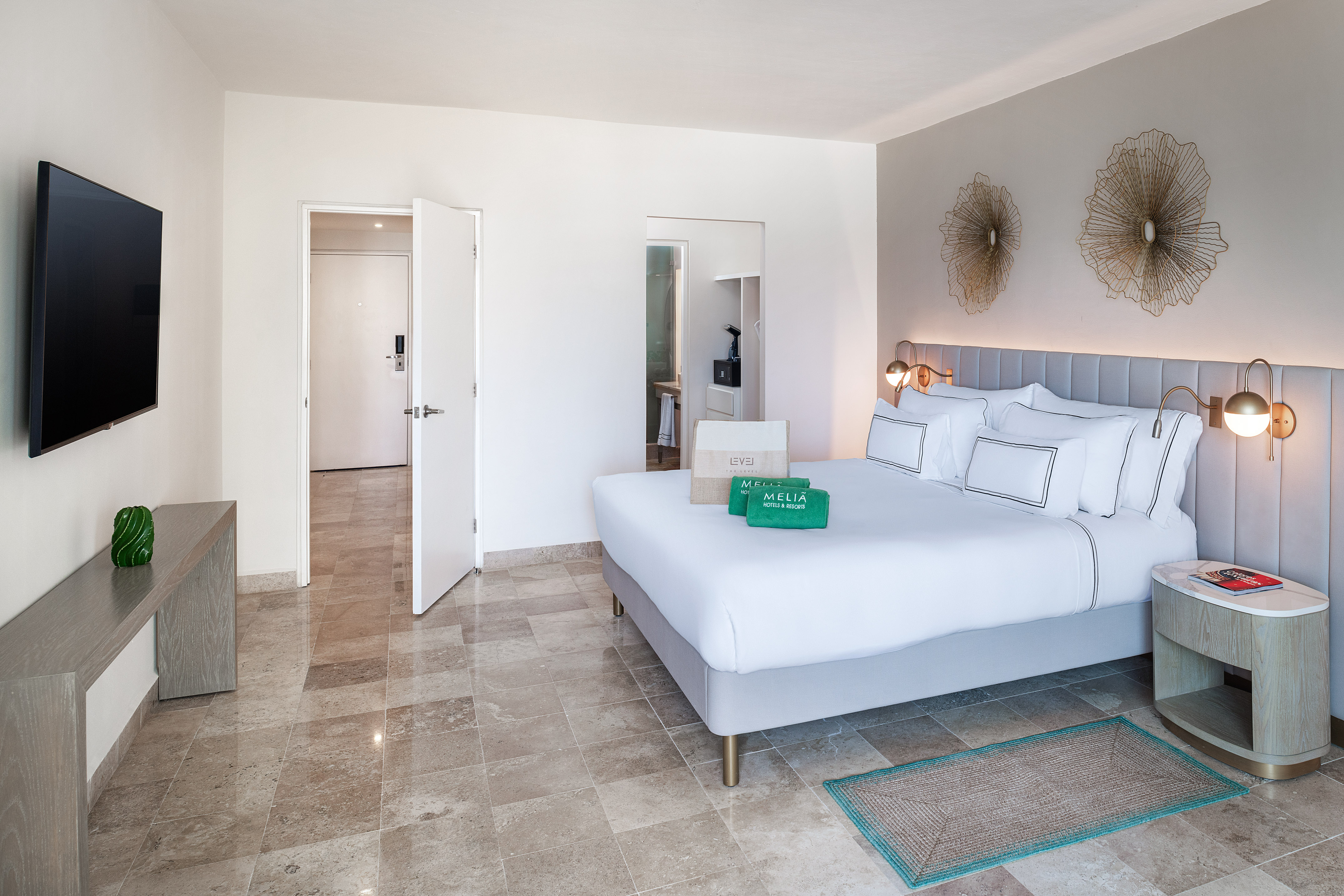 Modern Meliá hotel room with king bed, sleek headboard, wall TV, and tiled floor.