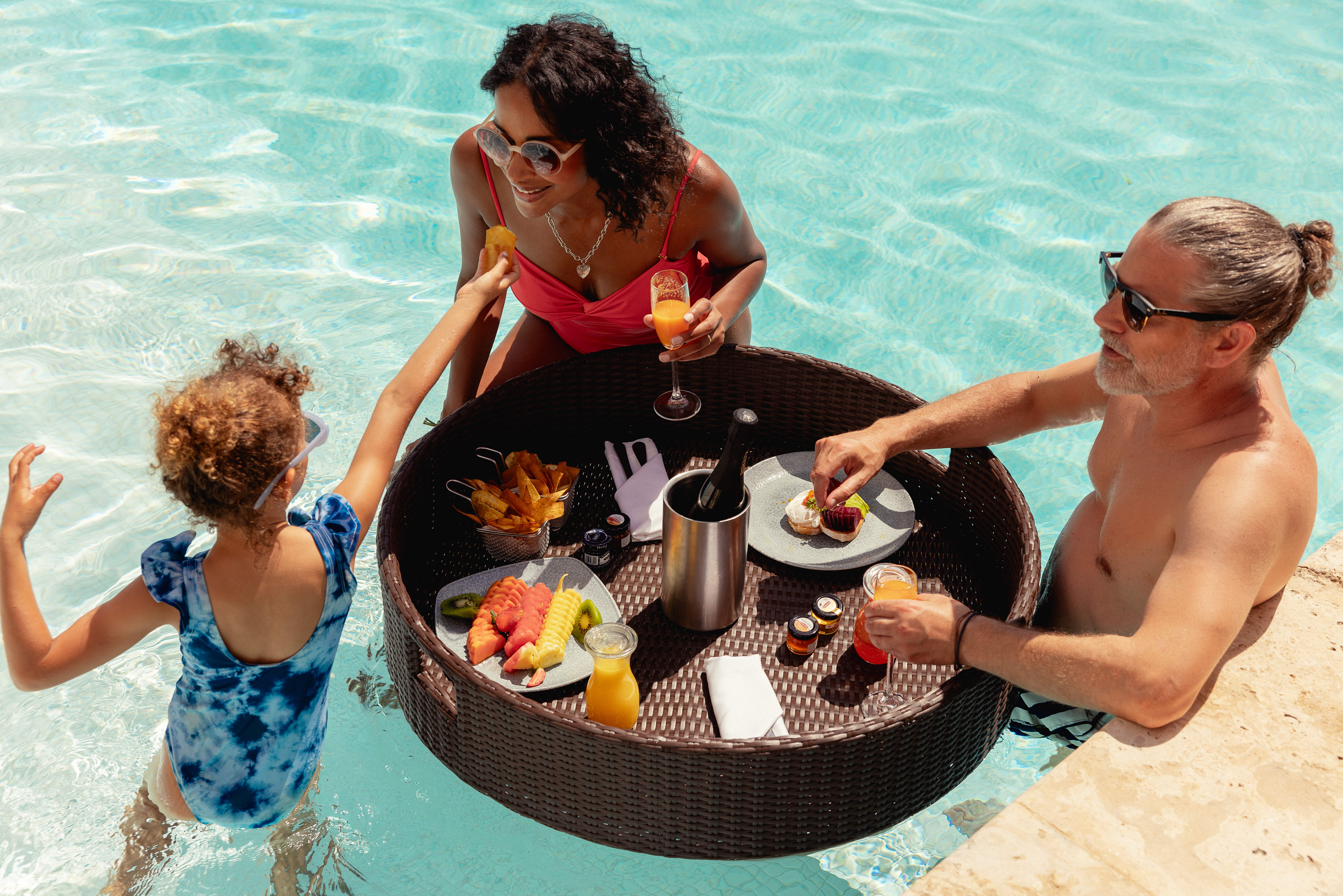 Parents and child enjoying floating breakfast in resort pool.