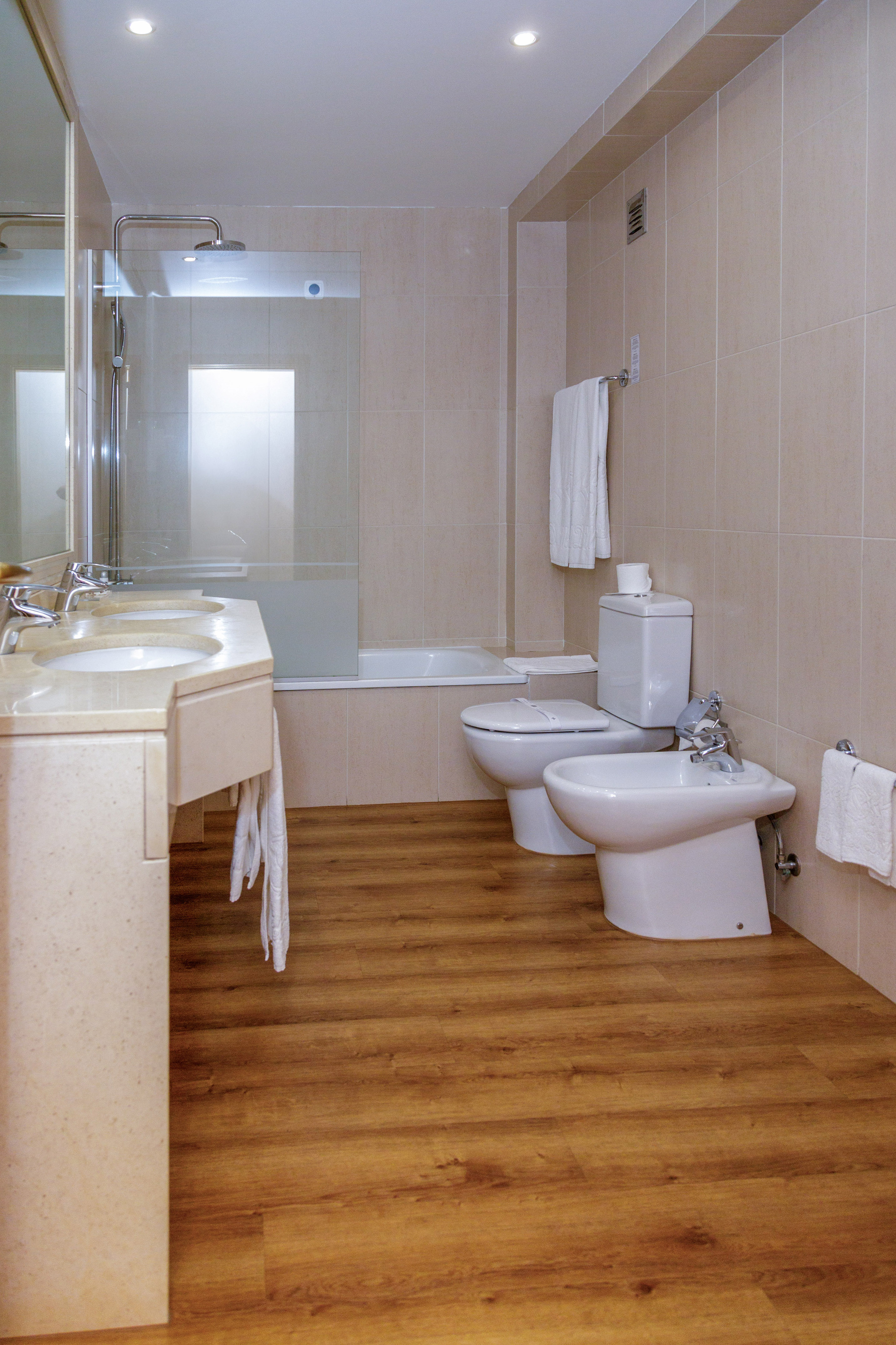 Modern hotel bathroom with double vanity, shower, bathtub, toilet, bidet, wood floor.