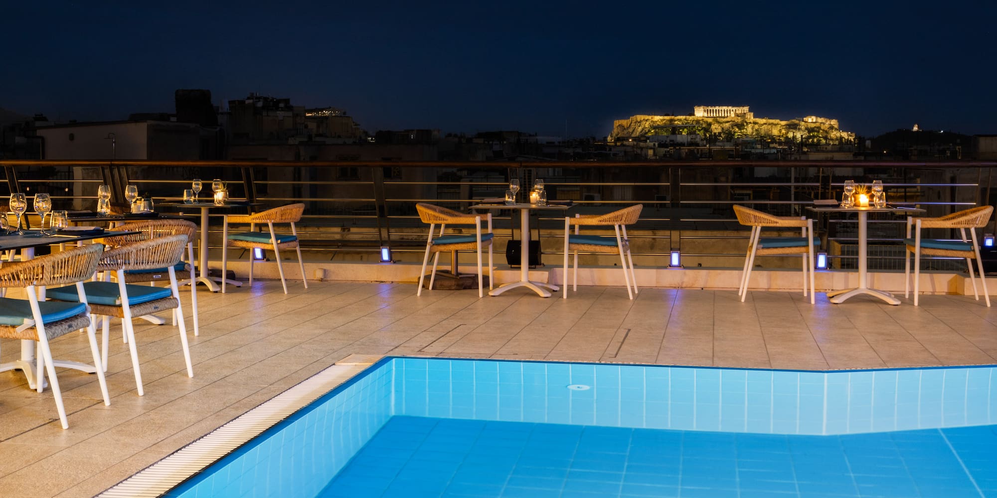 Athens rooftop pool bar with illuminated Acropolis view at night.