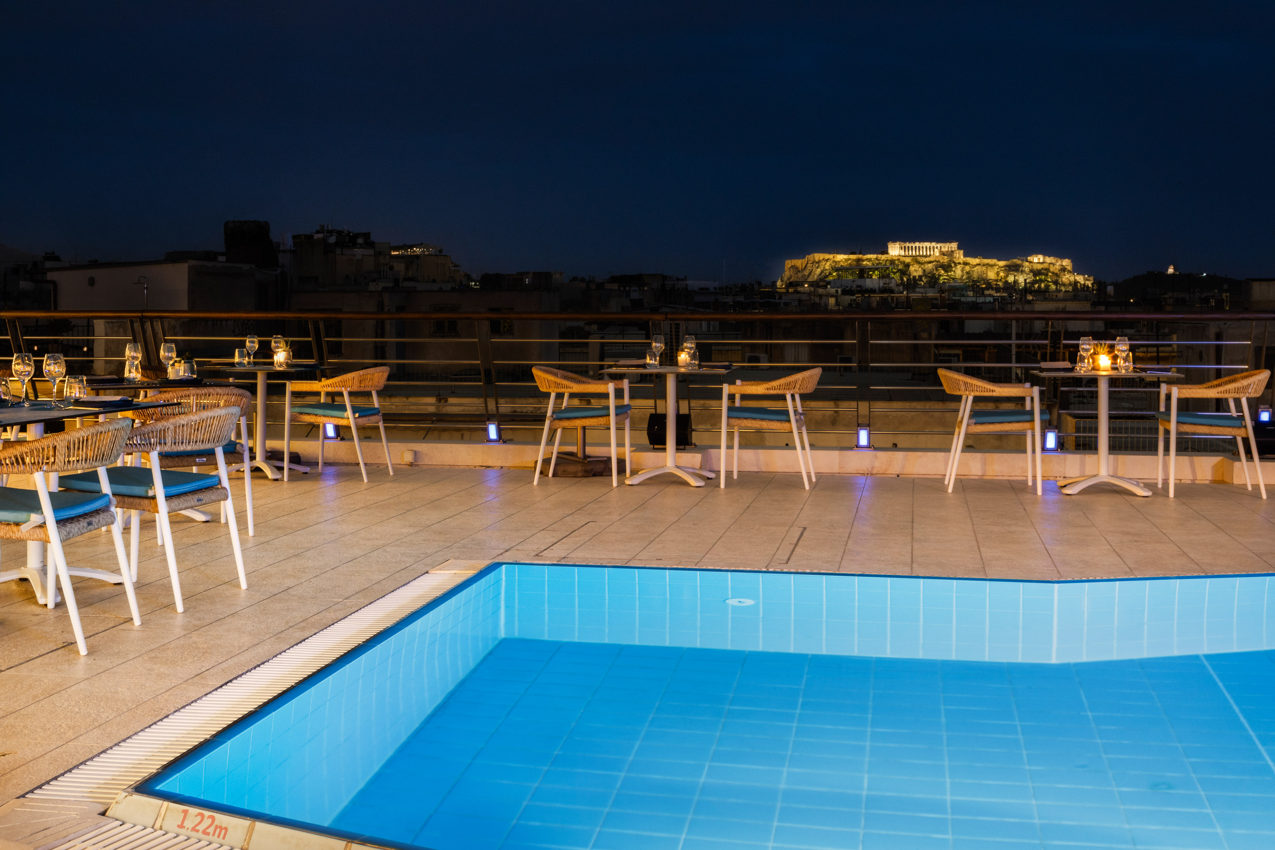 Athens rooftop pool bar with illuminated Acropolis view at night.