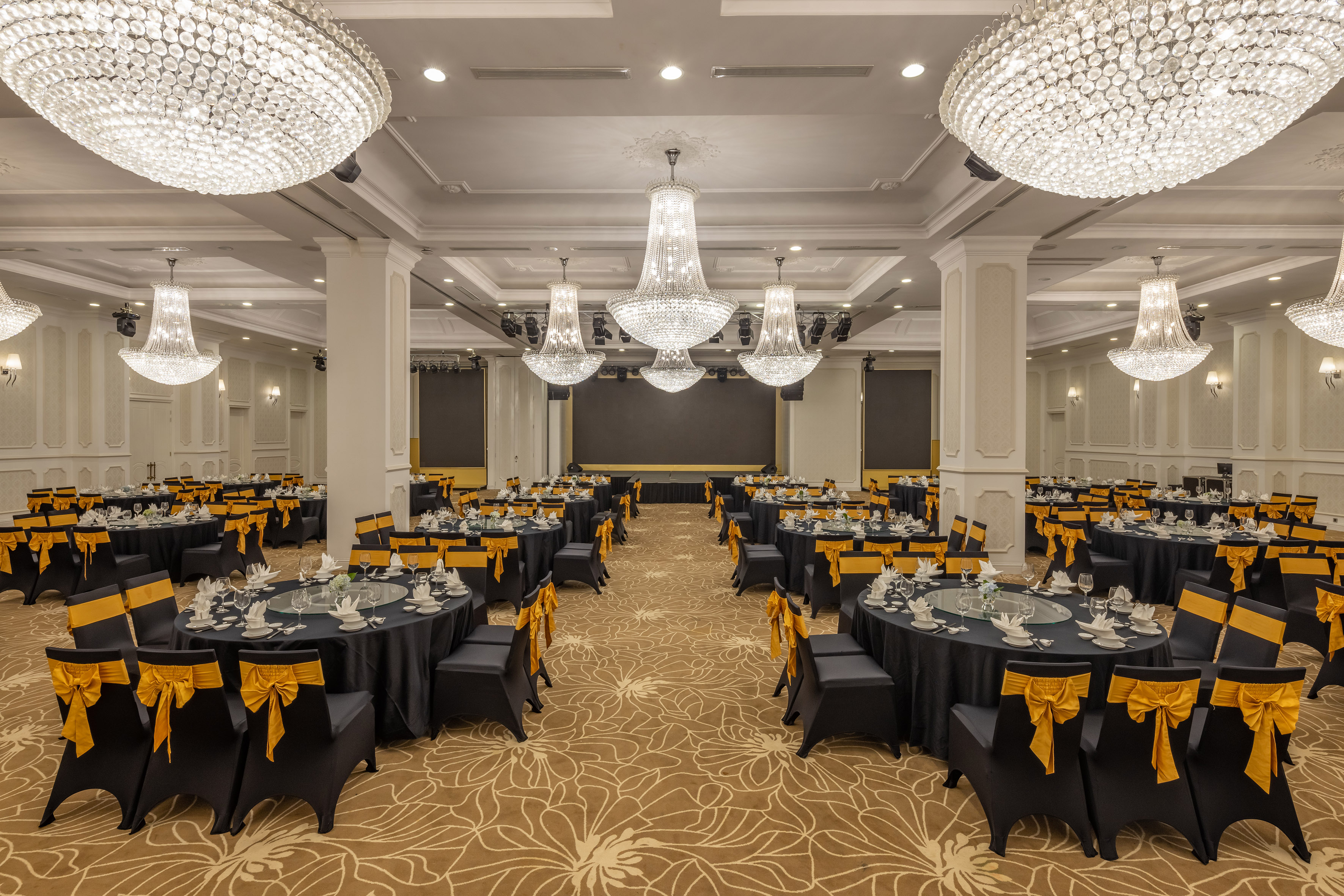 Elegant banquet hall with black and gold tables, ornate crystal chandeliers.