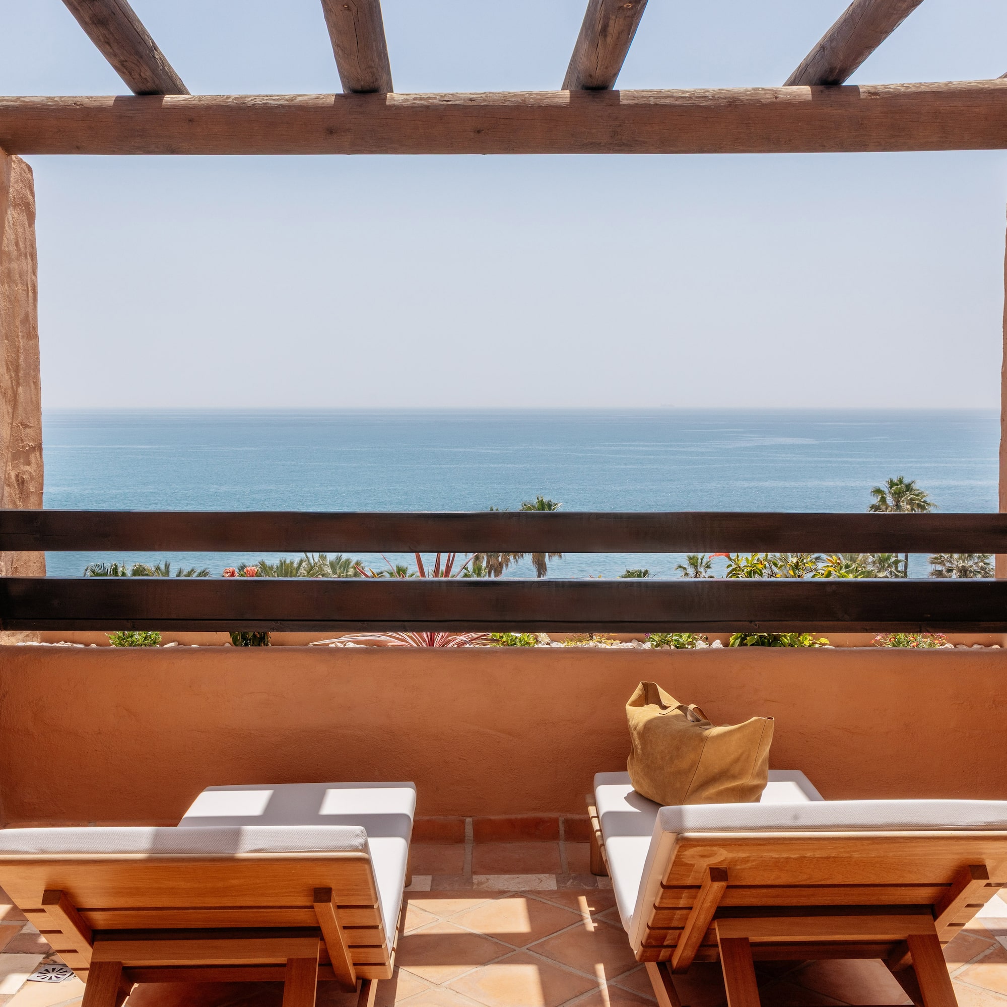 Resort balcony with ocean view, two wooden lounge chairs, and rustic pergola.