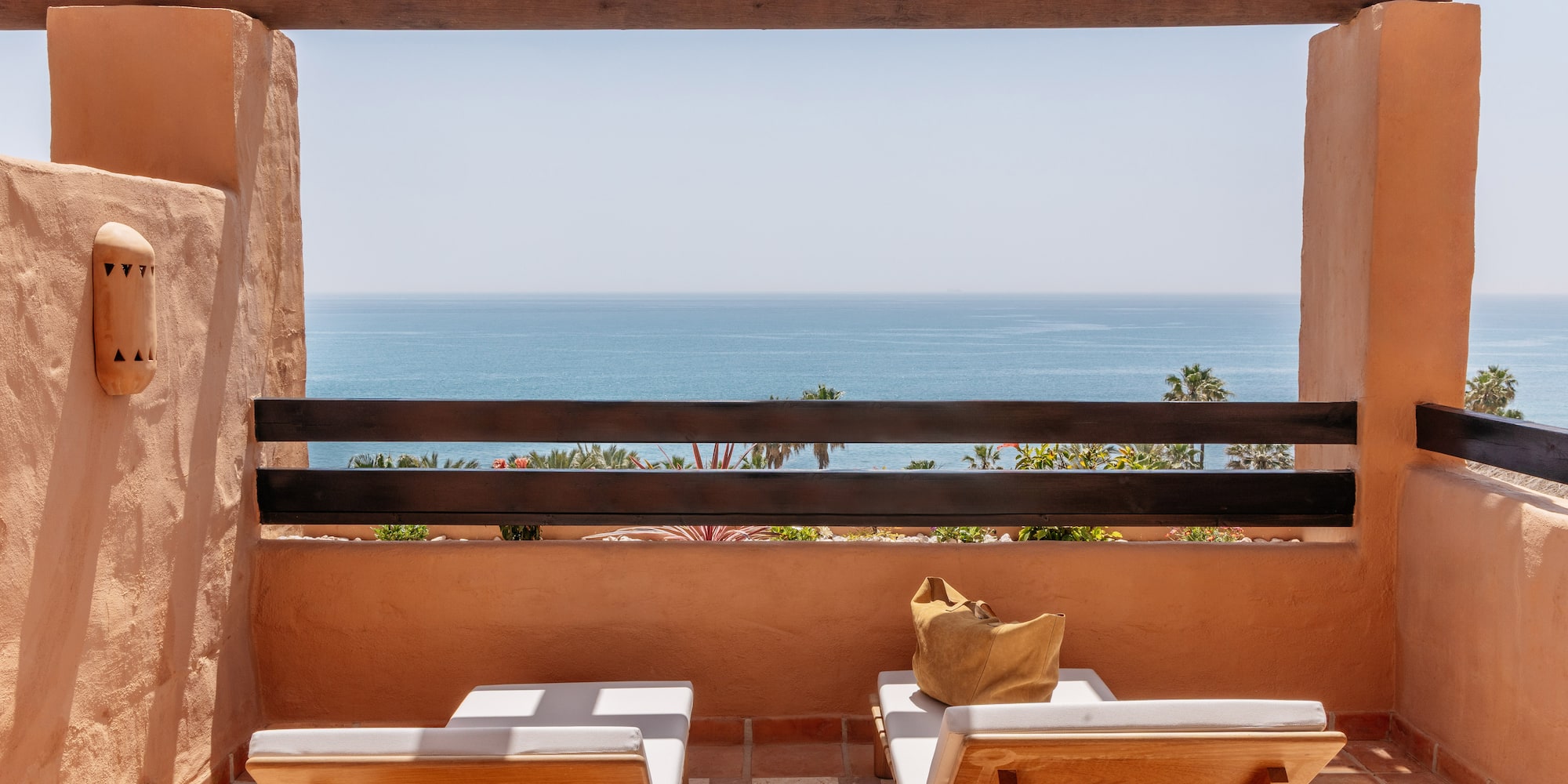 Resort balcony with ocean view, two wooden lounge chairs, and rustic pergola.