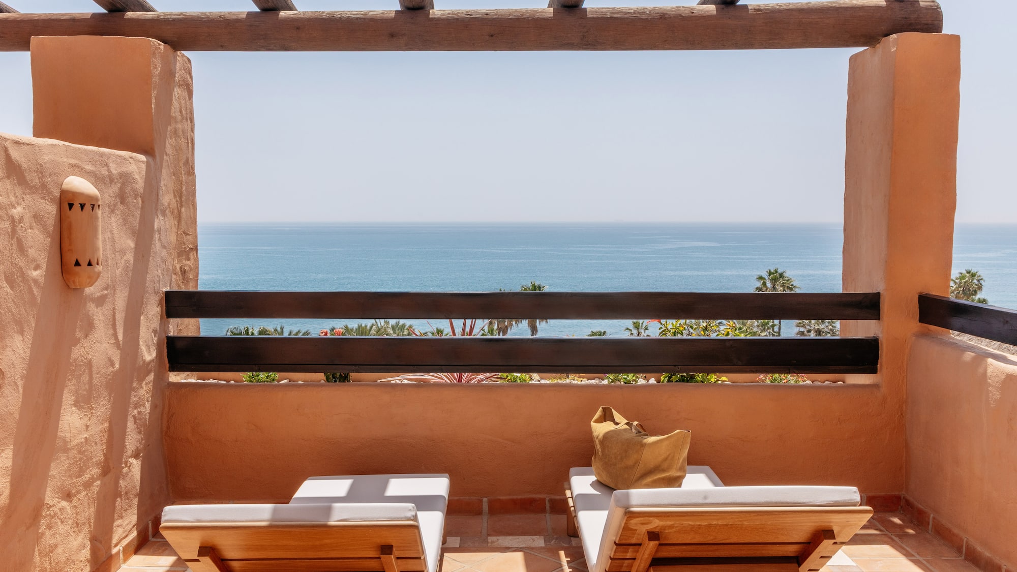 Resort balcony with ocean view, two wooden lounge chairs, and rustic pergola.
