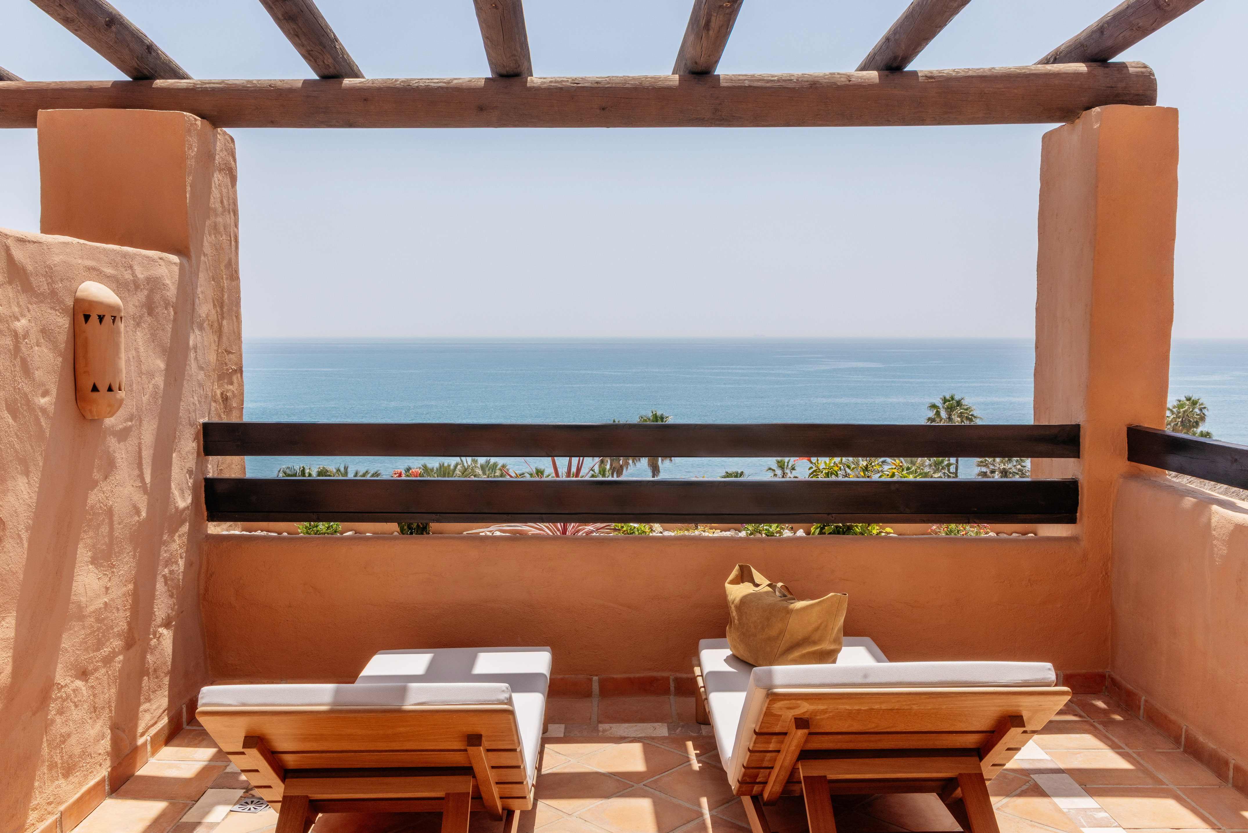Resort balcony with ocean view, two wooden lounge chairs, and rustic pergola.