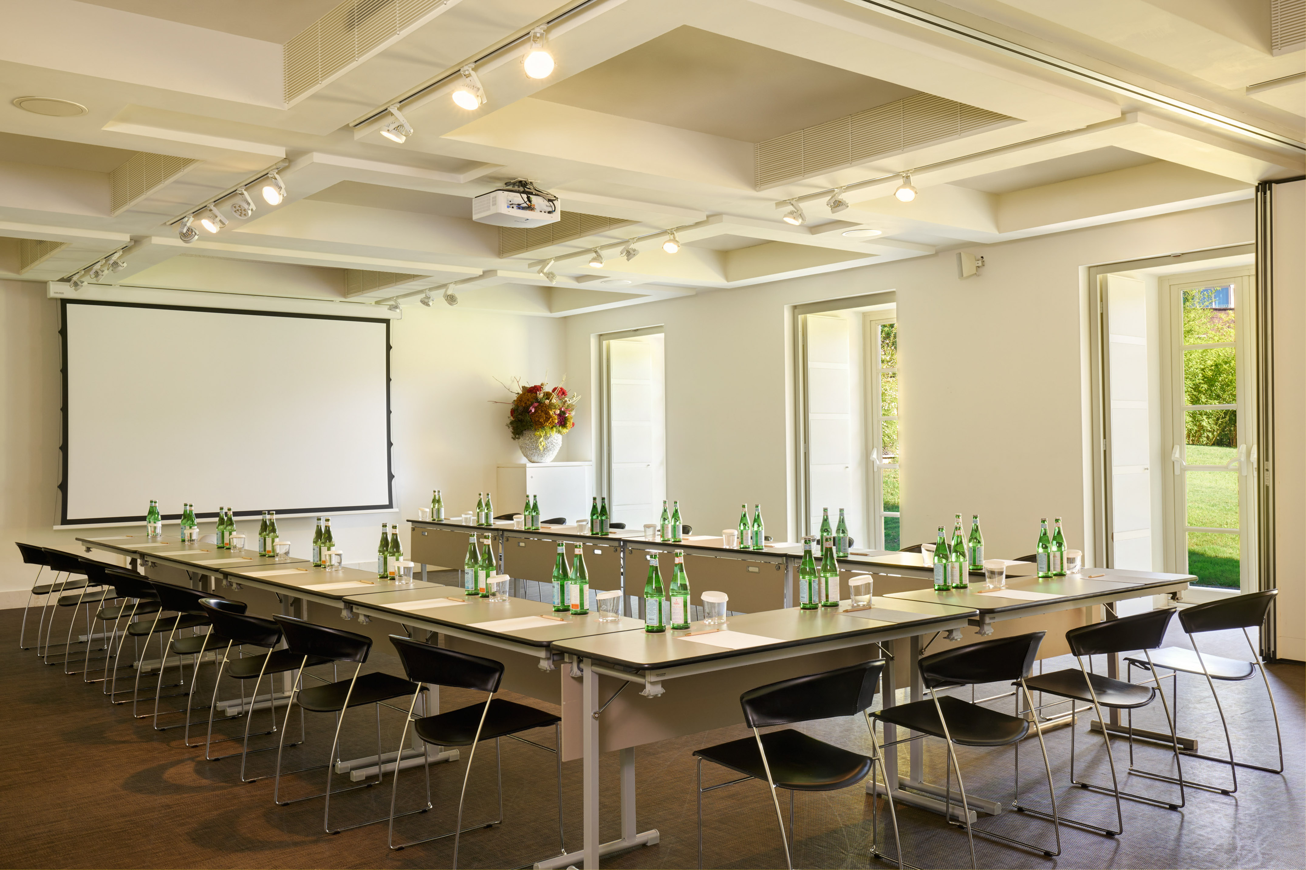 U-shaped conference room setup with projector screen, tables, and water bottles.