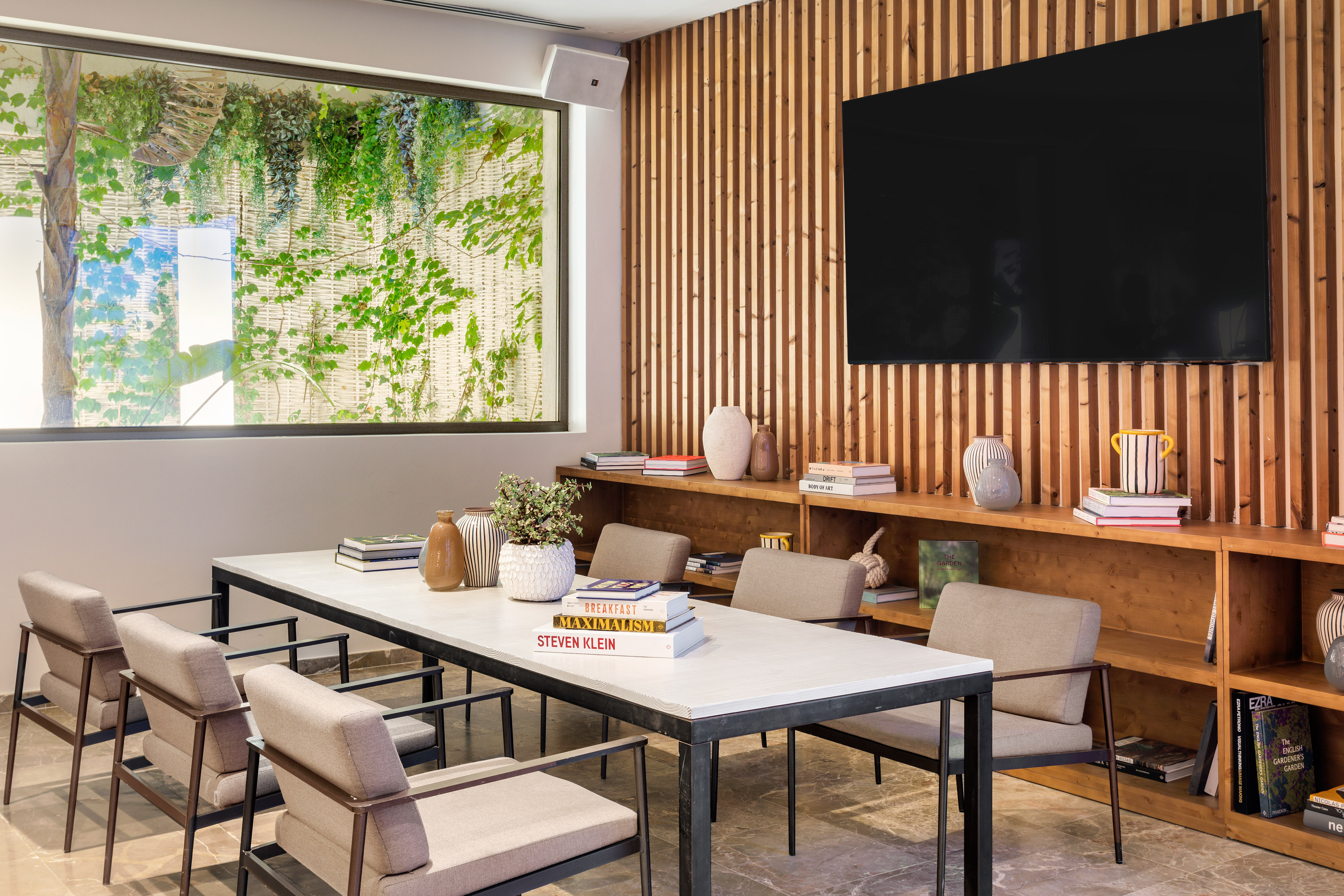 Modern meeting room with table, chairs, wooden wall, TV, and green window view.