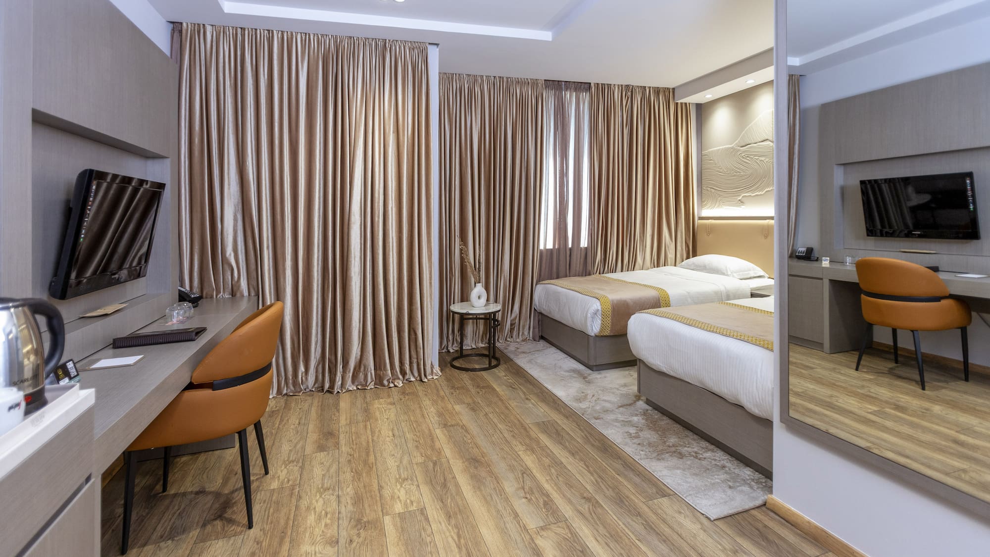 Modern hotel twin room with wood floor, desk, TV, and beige curtains.
