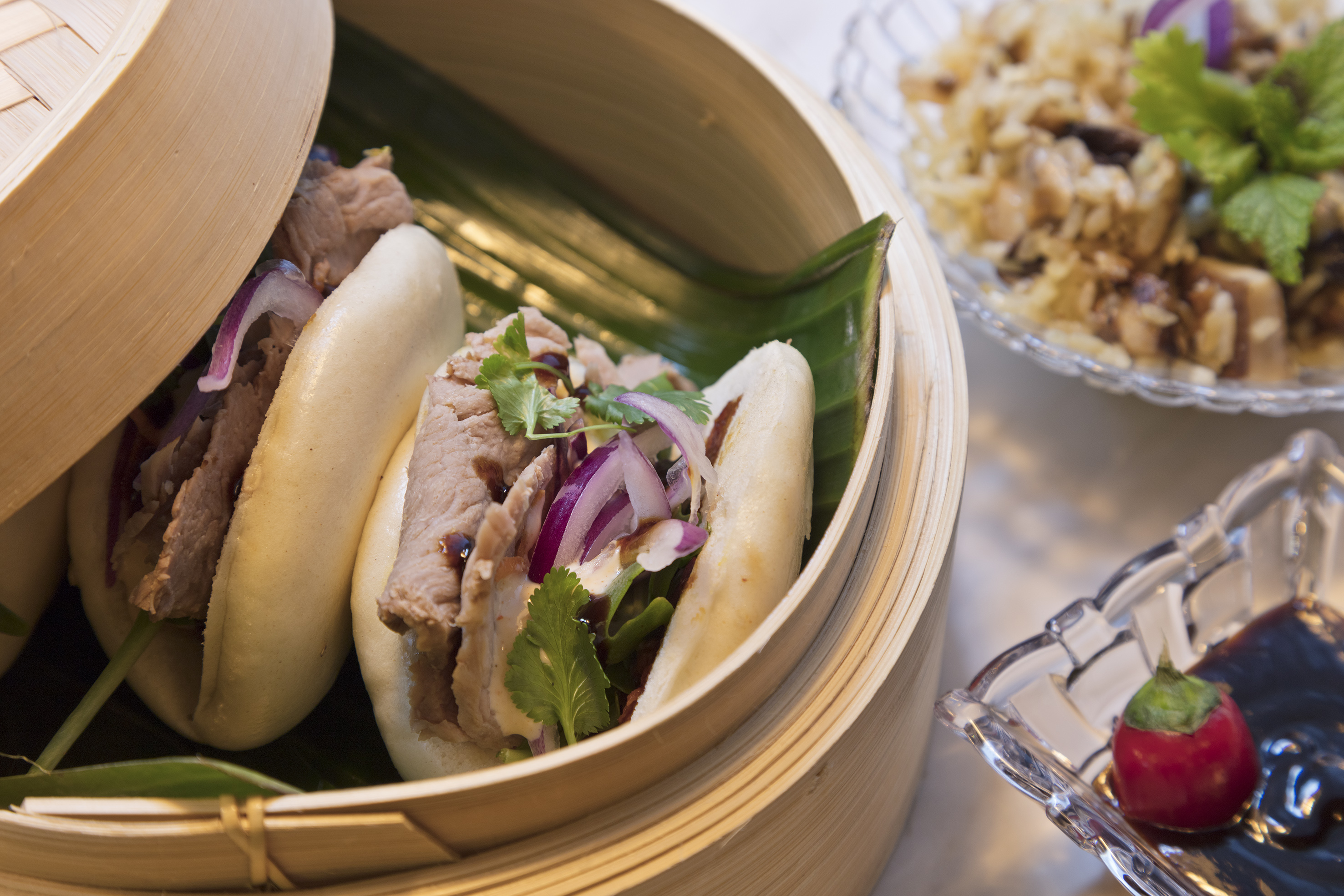 Pork bao buns with red onion and cilantro in a bamboo steamer.