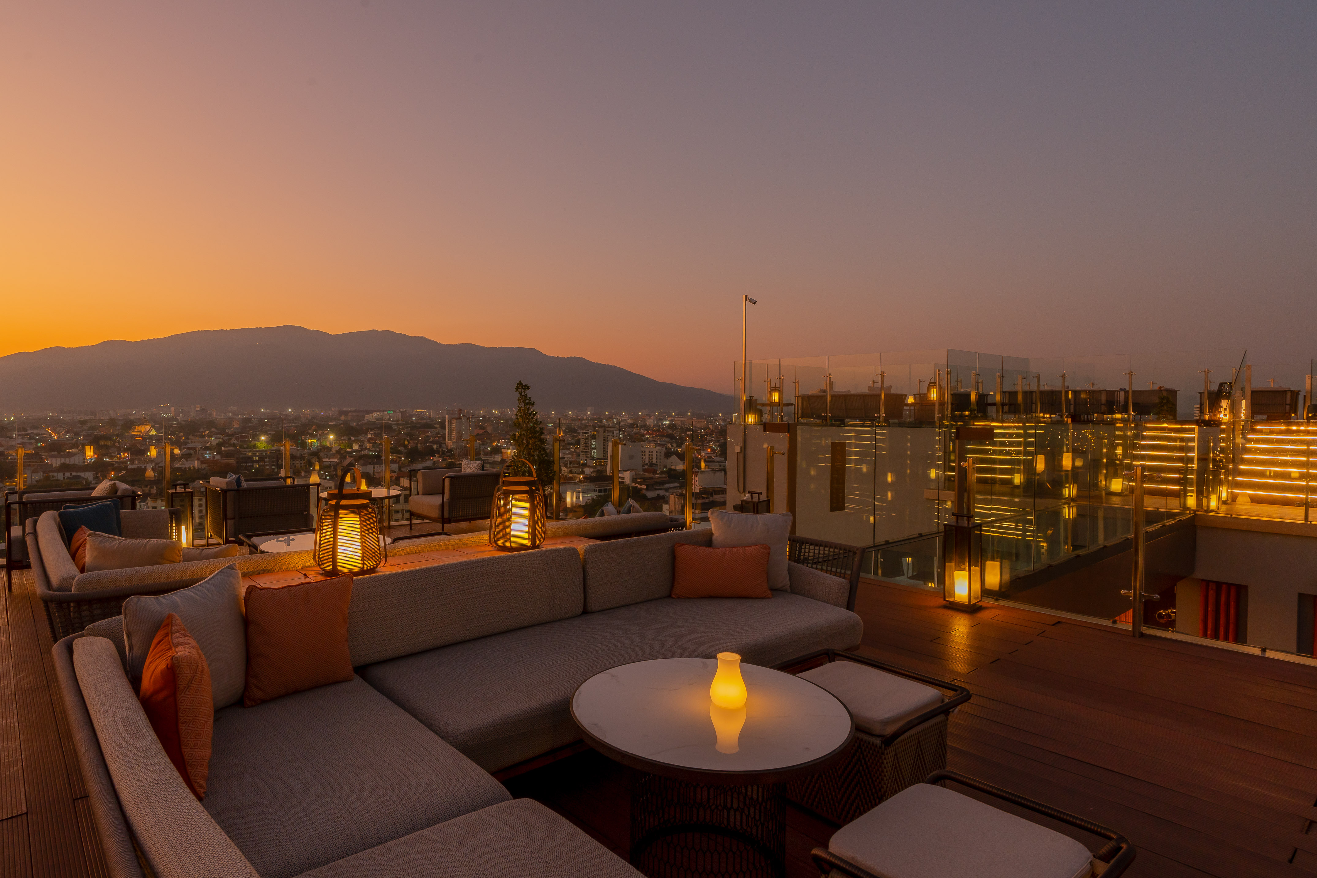 Sunset rooftop lounge overlooking city and mountains with ambient lighting.