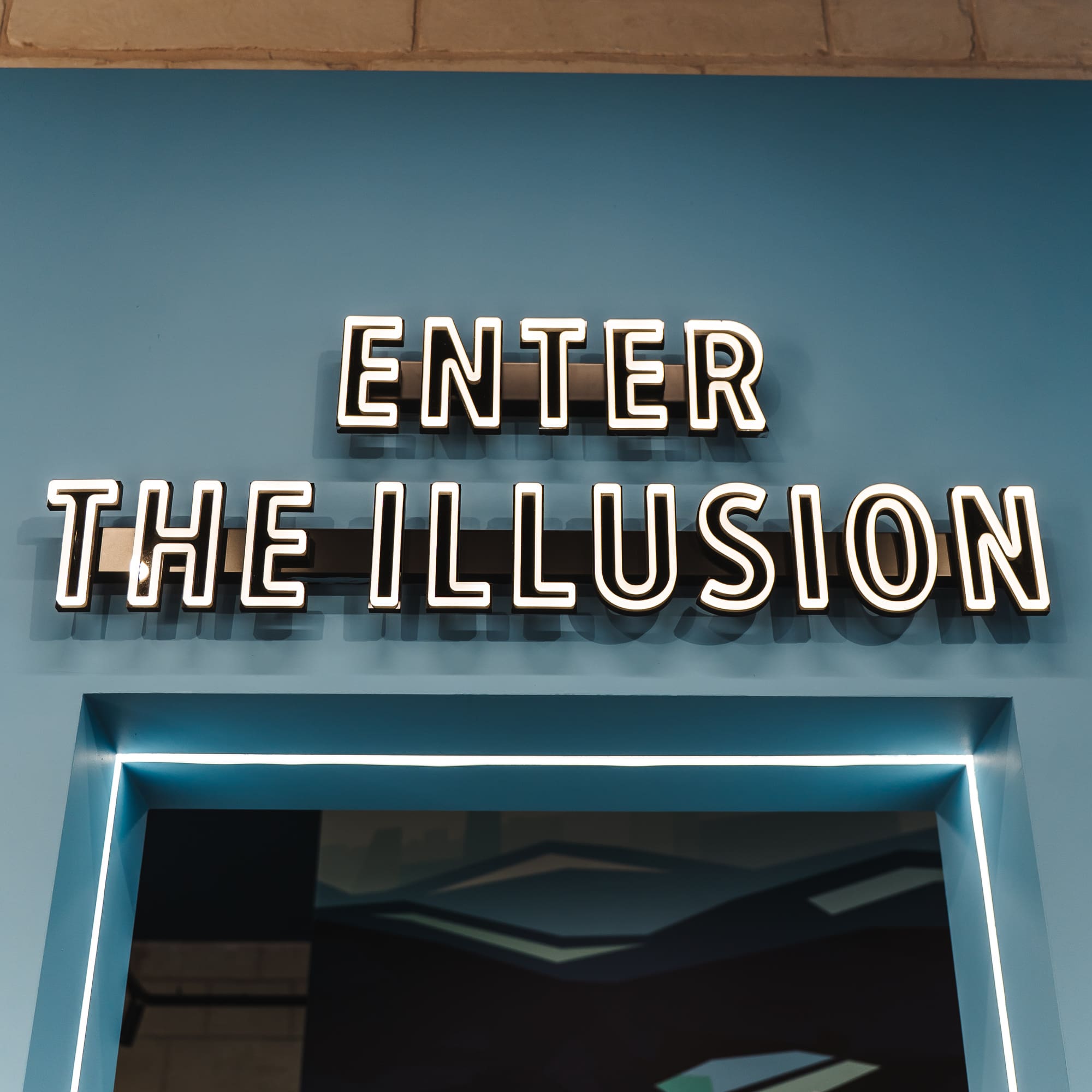 Neon sign 'ENTER THE ILLUSION' on blue wall above LED-lit entrance.