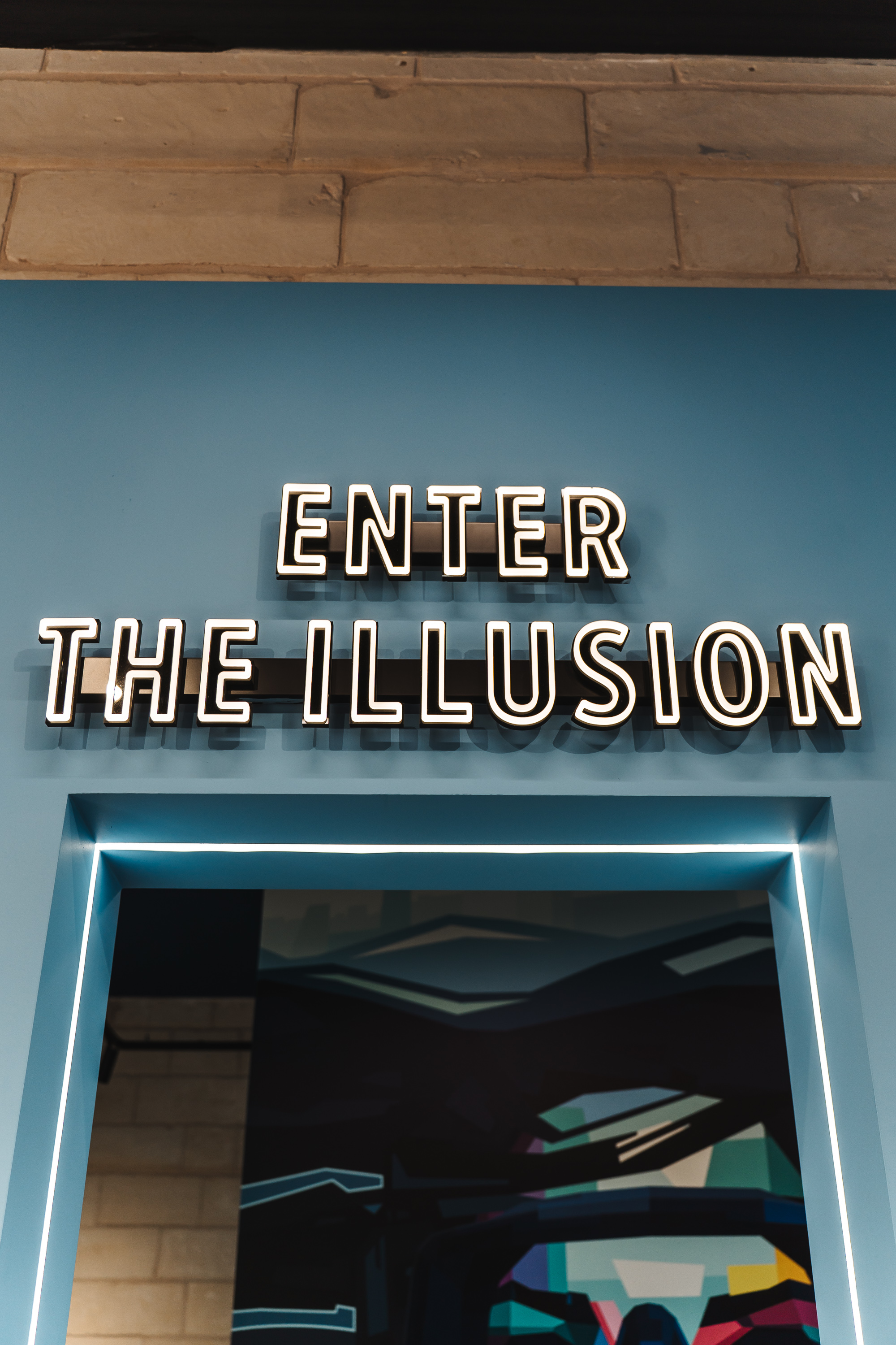 Neon sign 'ENTER THE ILLUSION' on blue wall above LED-lit entrance.