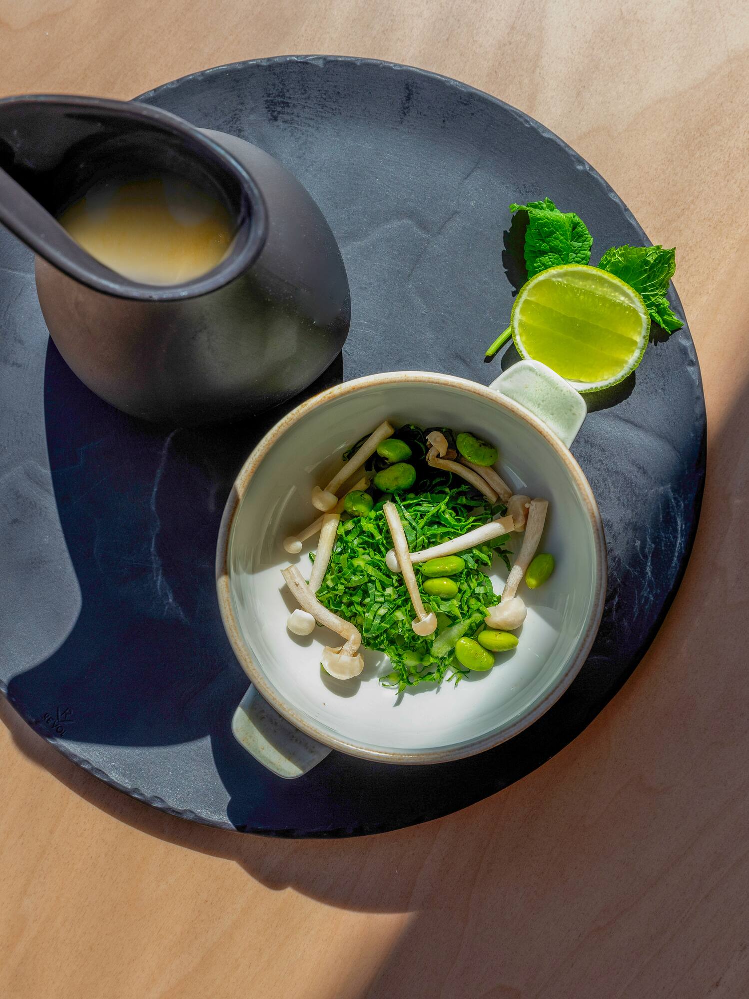 Greens, mushrooms, edamame, lime, and creamy sauce on a dark plate.