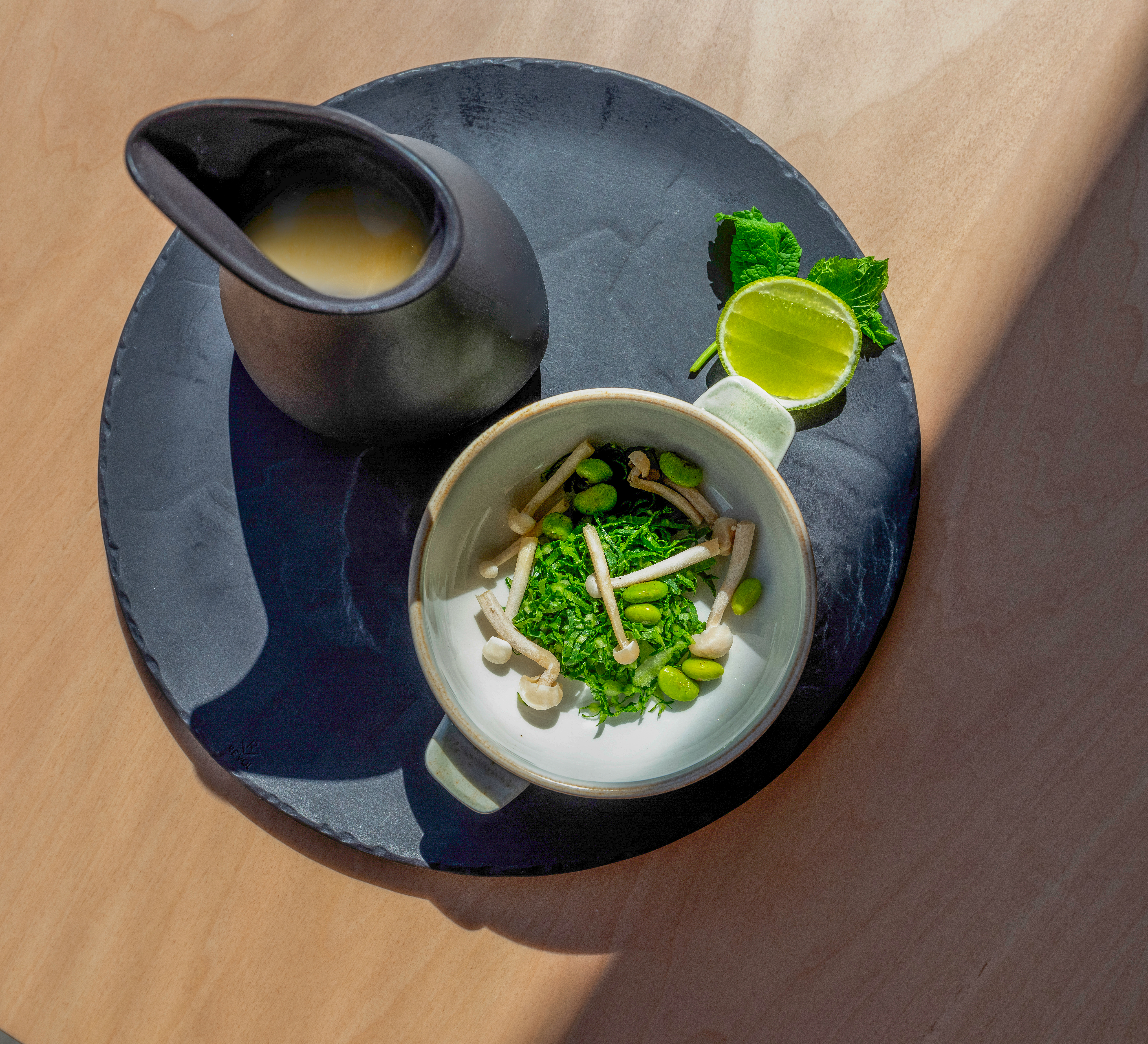 Greens, mushrooms, edamame, lime, and creamy sauce on a dark plate.