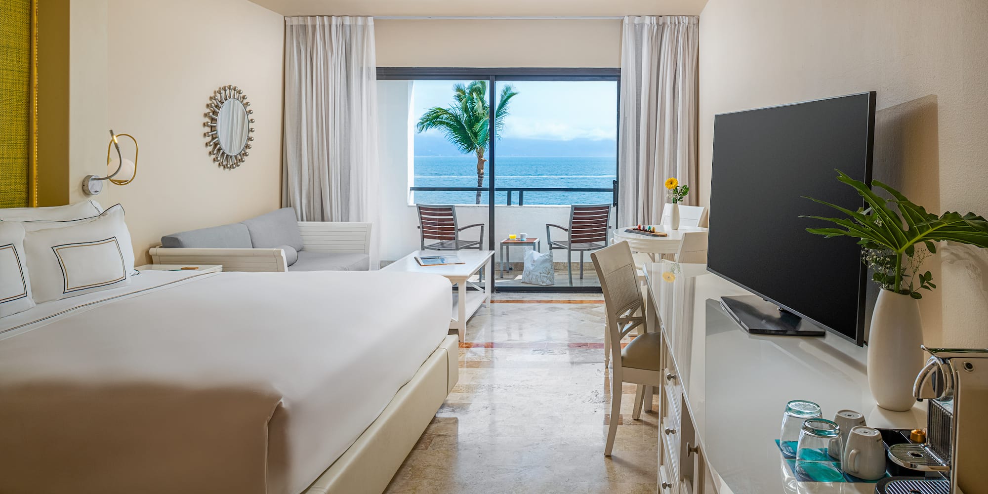 Luxury resort room with ocean view balcony, king bed, and palm tree.