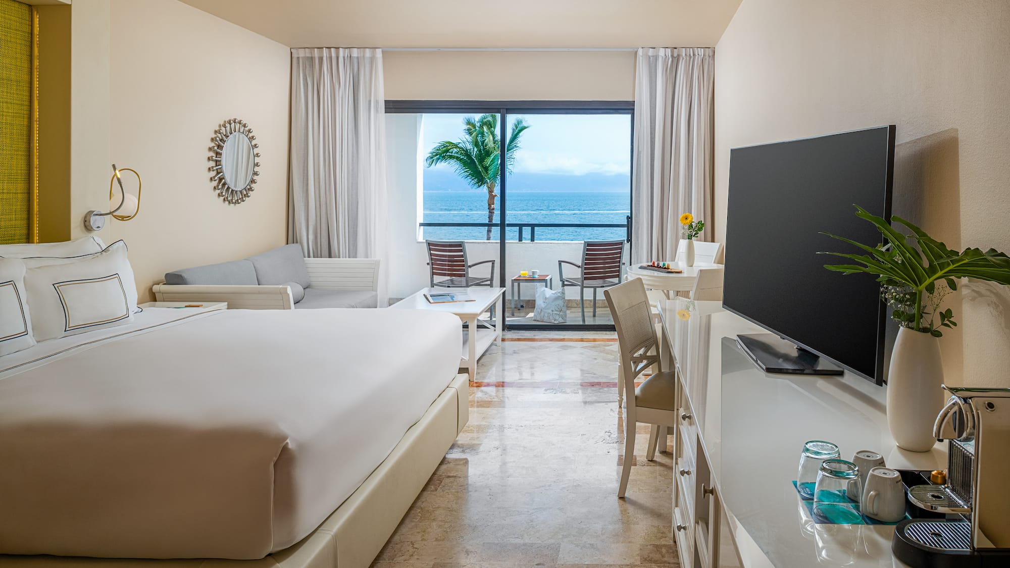 Tropical ocean view hotel suite with balcony, king bed, and modern decor.