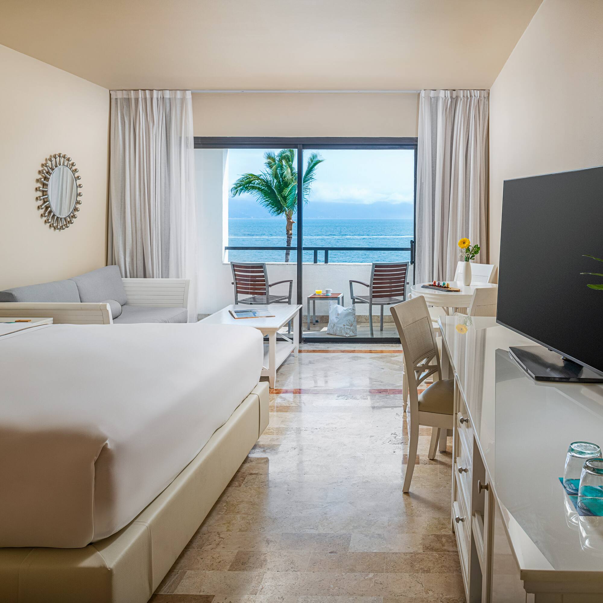 Tropical ocean view hotel suite with balcony, king bed, and modern decor.