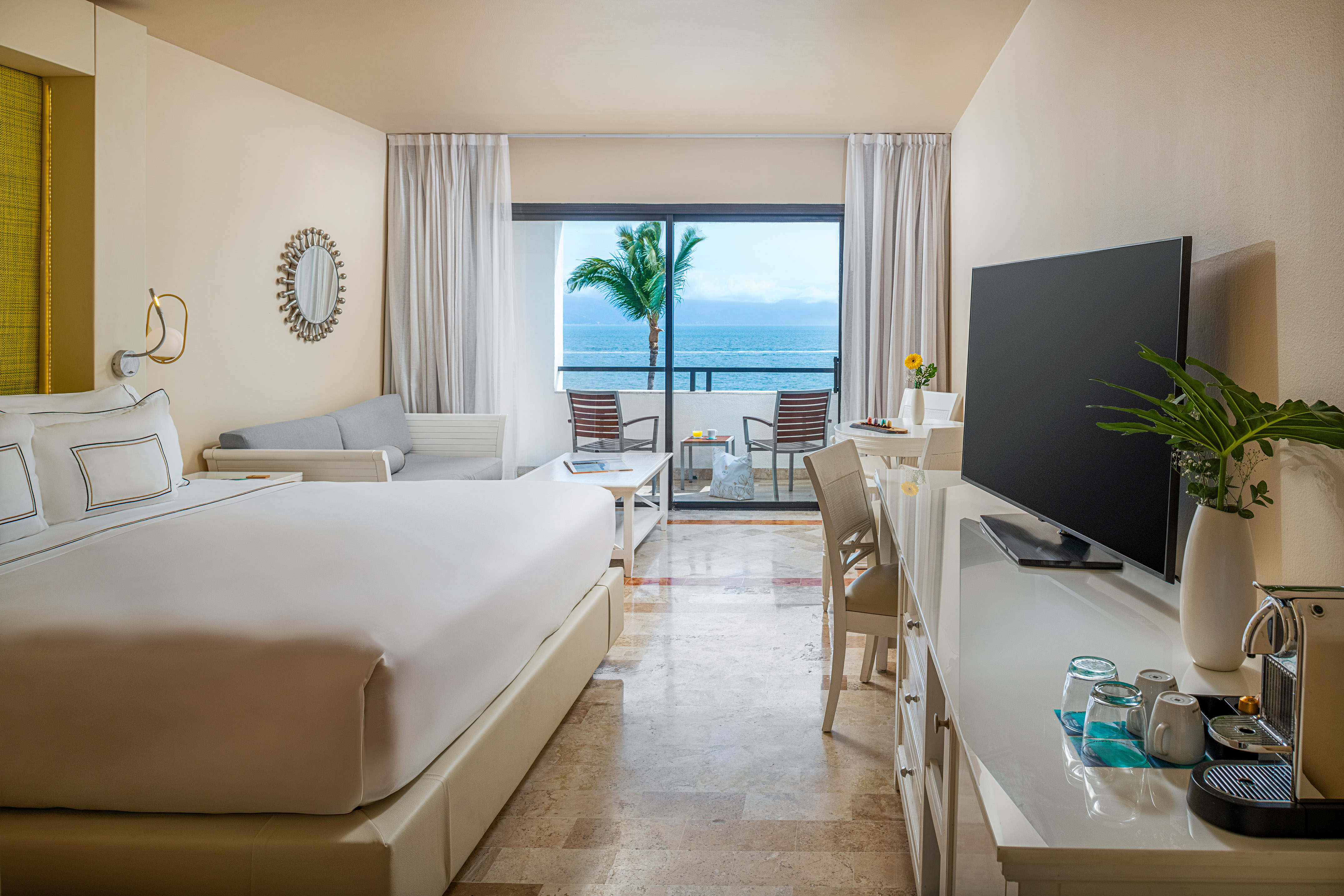 Luxury resort room with ocean view balcony, king bed, and palm tree.