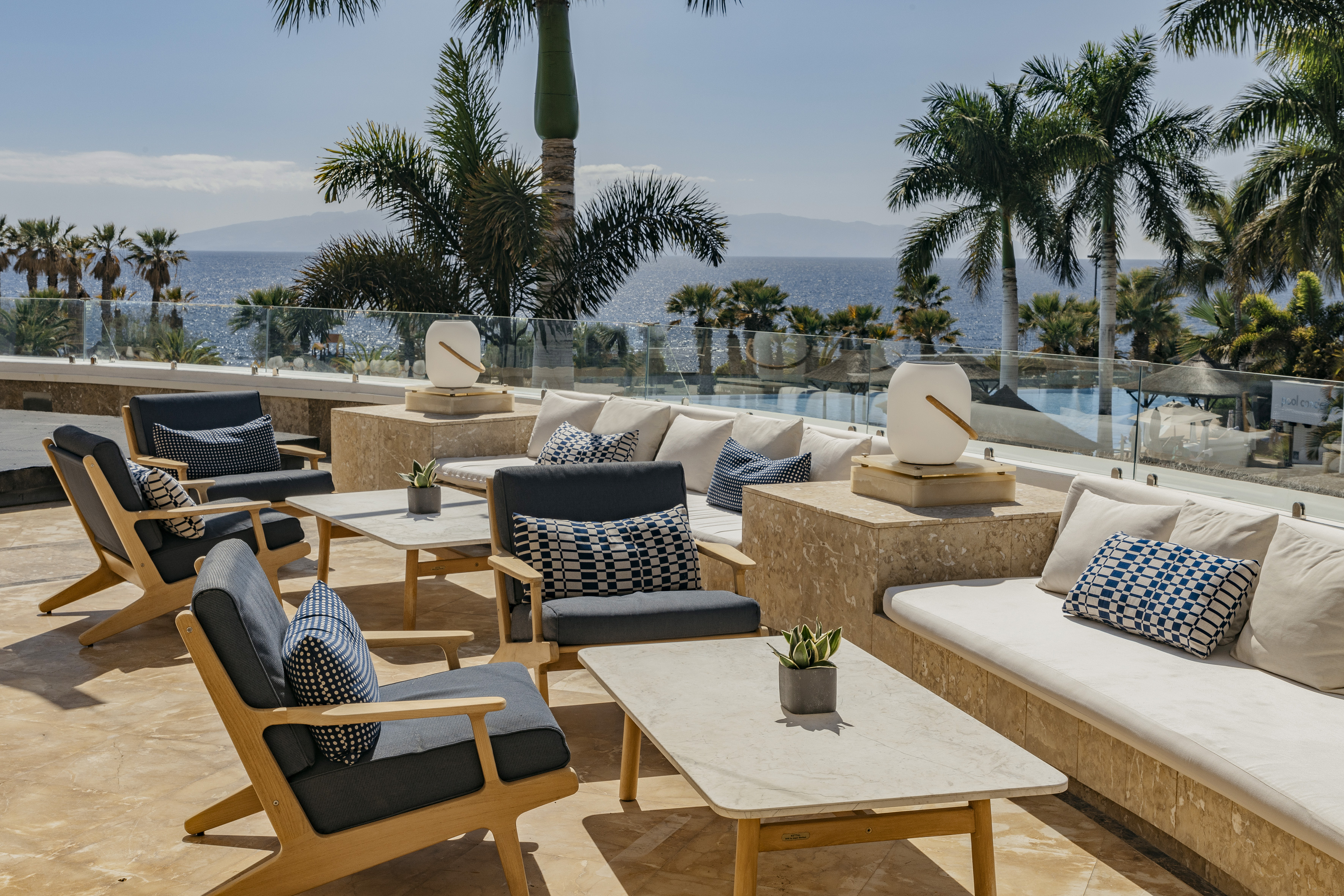Sunny hotel terrace with ocean view, modern outdoor furniture and palm trees.