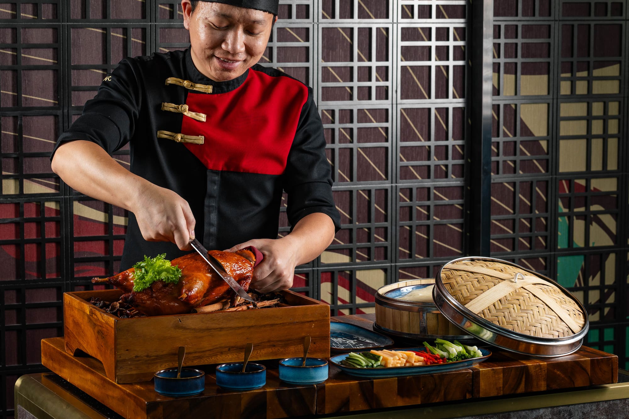 Chef carving glossy Peking duck, accompanied by pancakes and condiments.