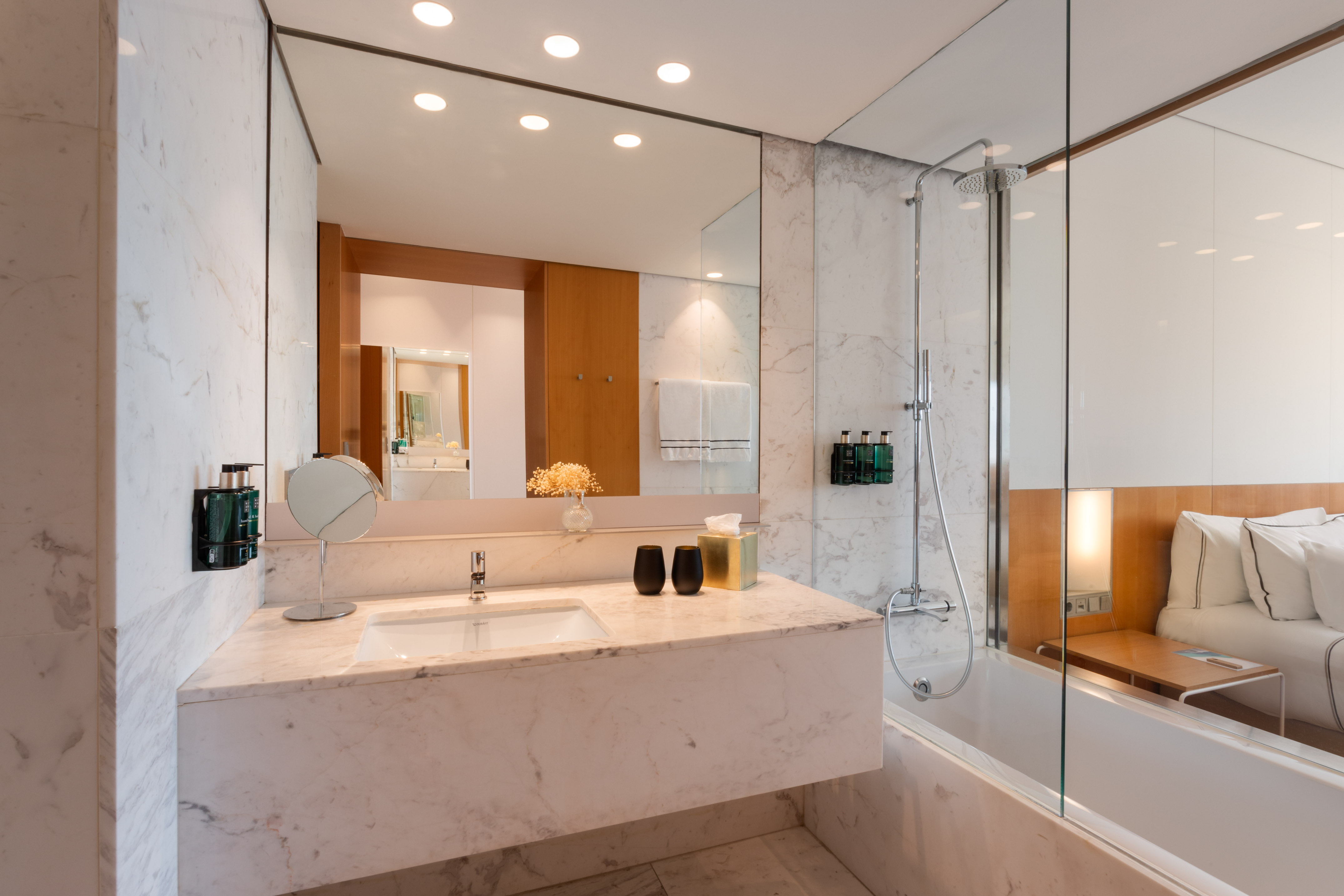 Modern marble bathroom with vanity, shower, and view into the bedroom.